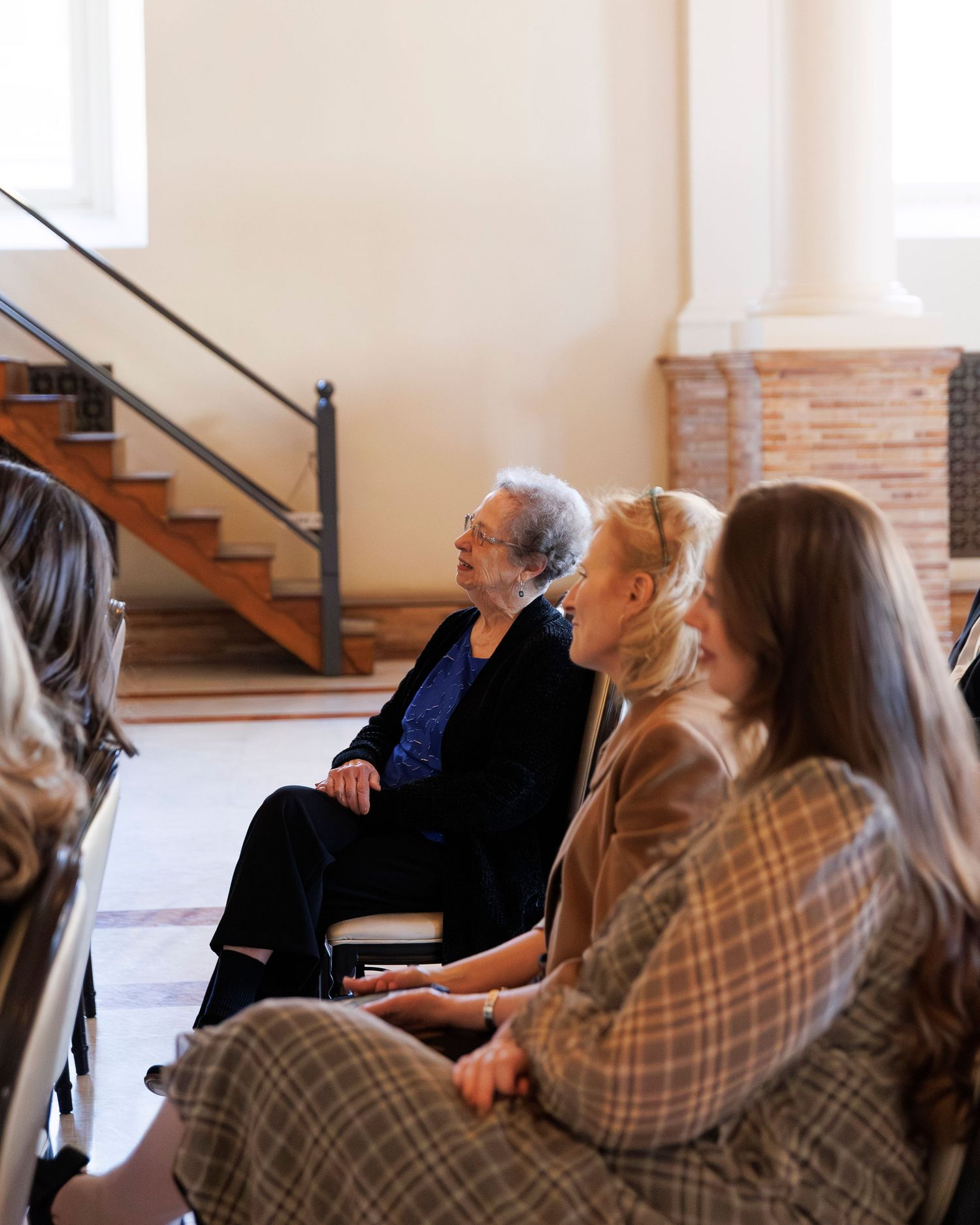 Wedding guests seated in rows watching a ceremony in an indoor venue with wooden stairs.