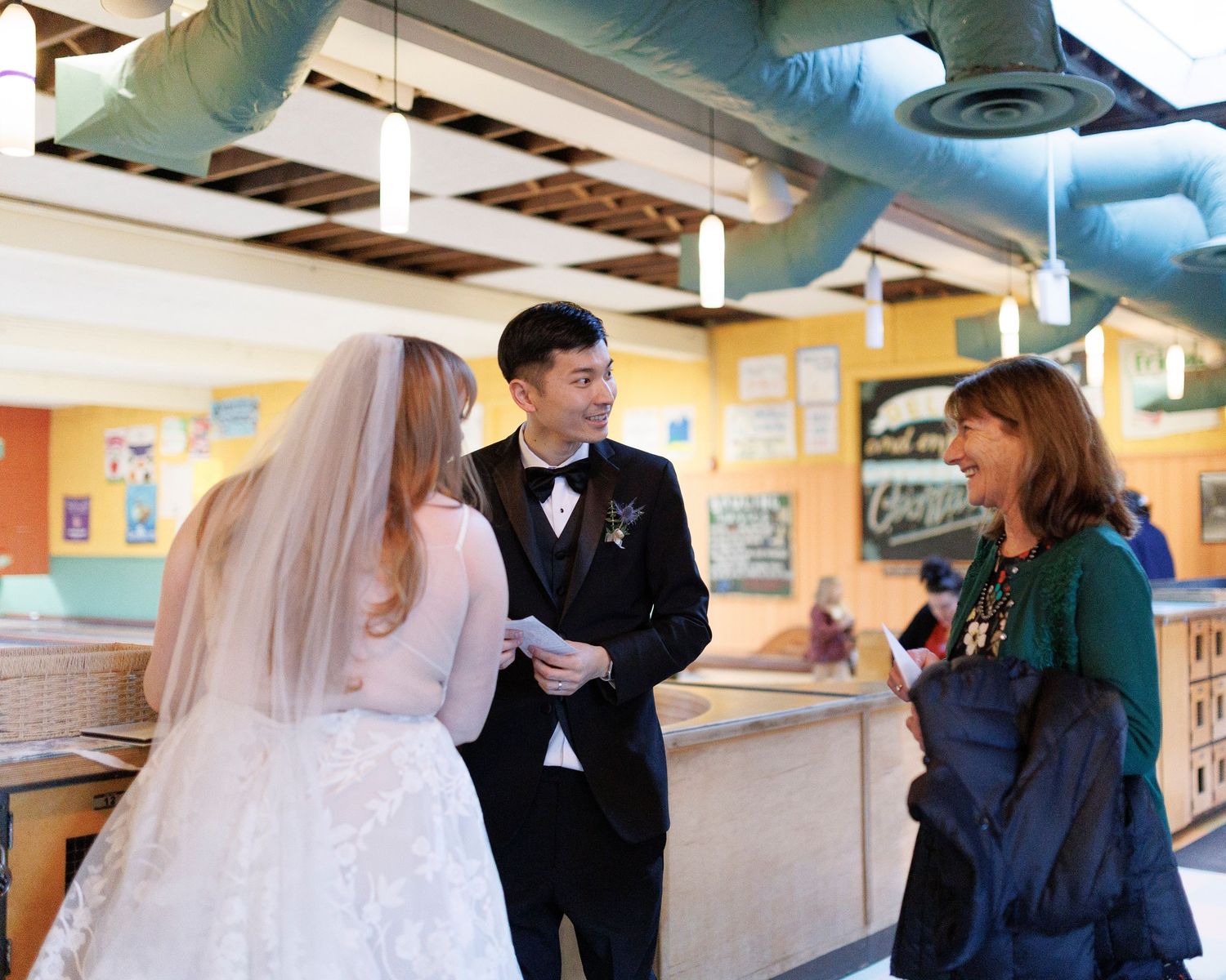 A wedding couple and their guests browse through displays at what appears to be an art gallery or exhibition space.