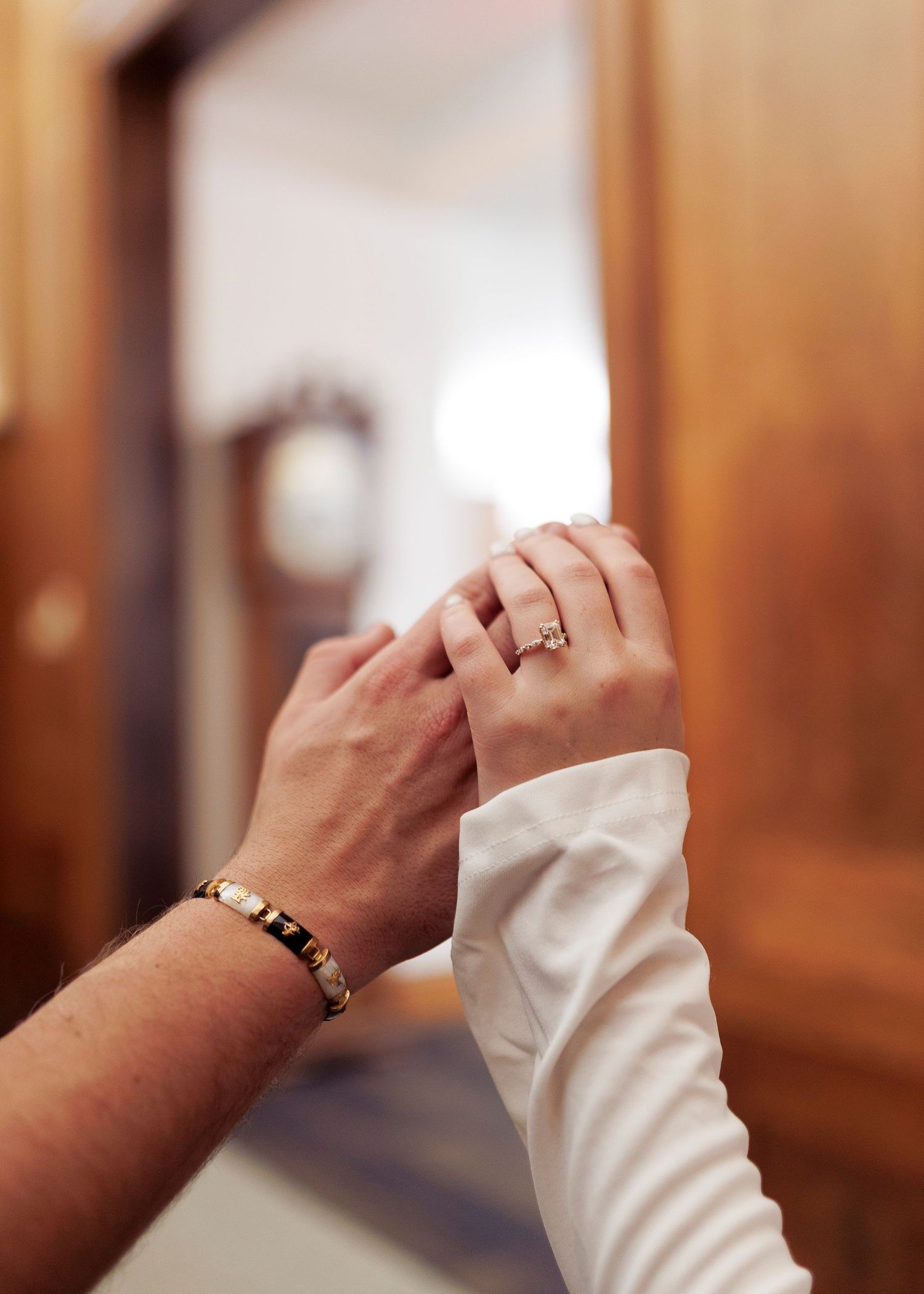 A hand wearing a white sleeve and ring reaches out against a warm-toned wooden background.