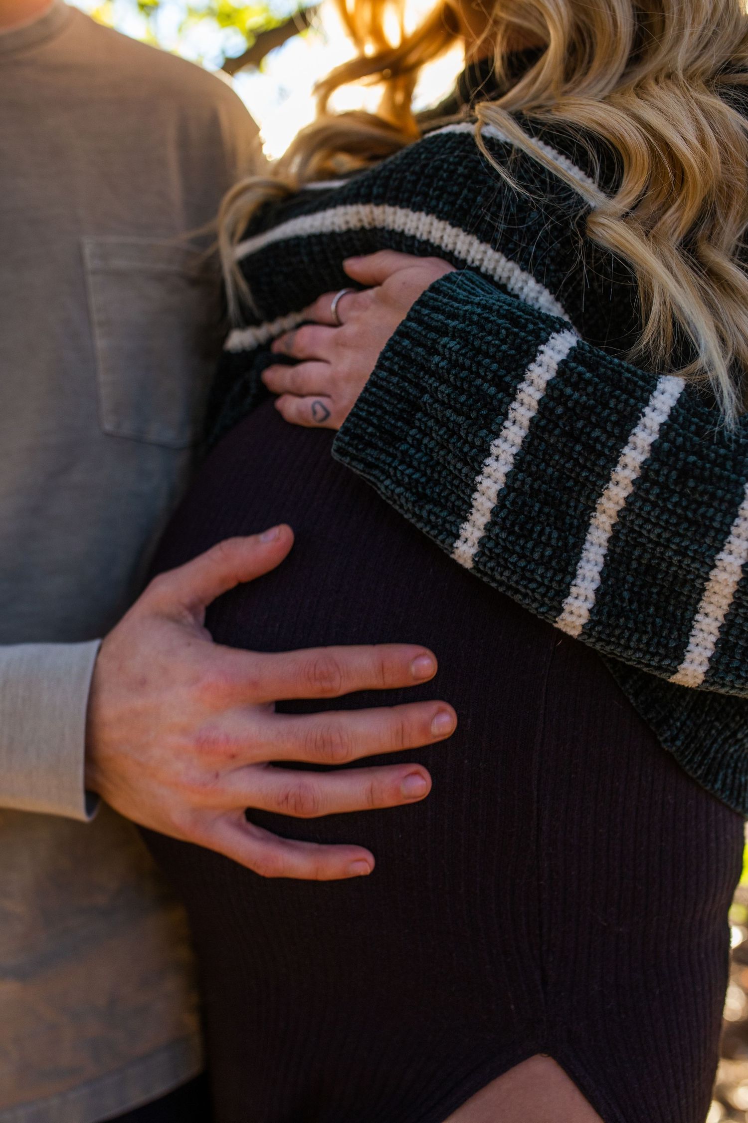 A hand gently rests on a person's shoulder wearing a dark knit sweater with gray stripes.