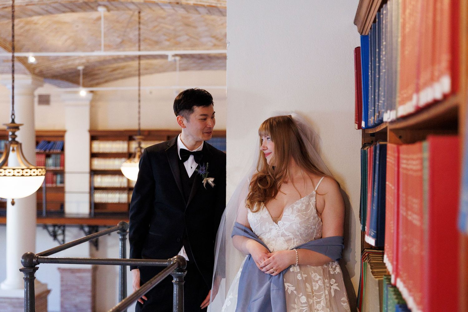 Couple in formal attire shares intimate moments while browsing books in library stacks.