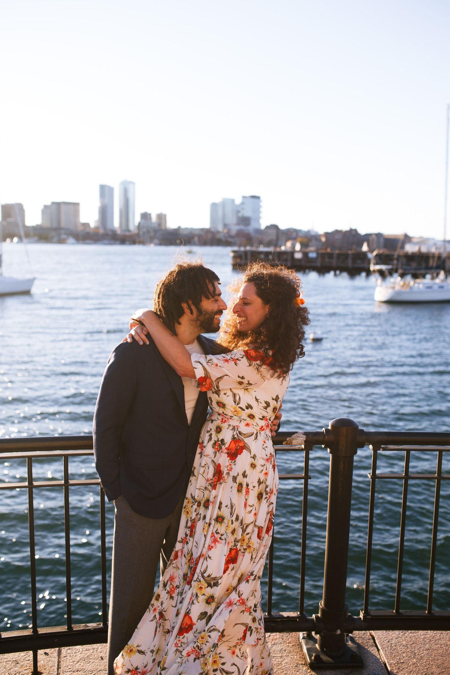 A couple enjoys a romantic moment by the waterfront with the city skyline visible in the background.