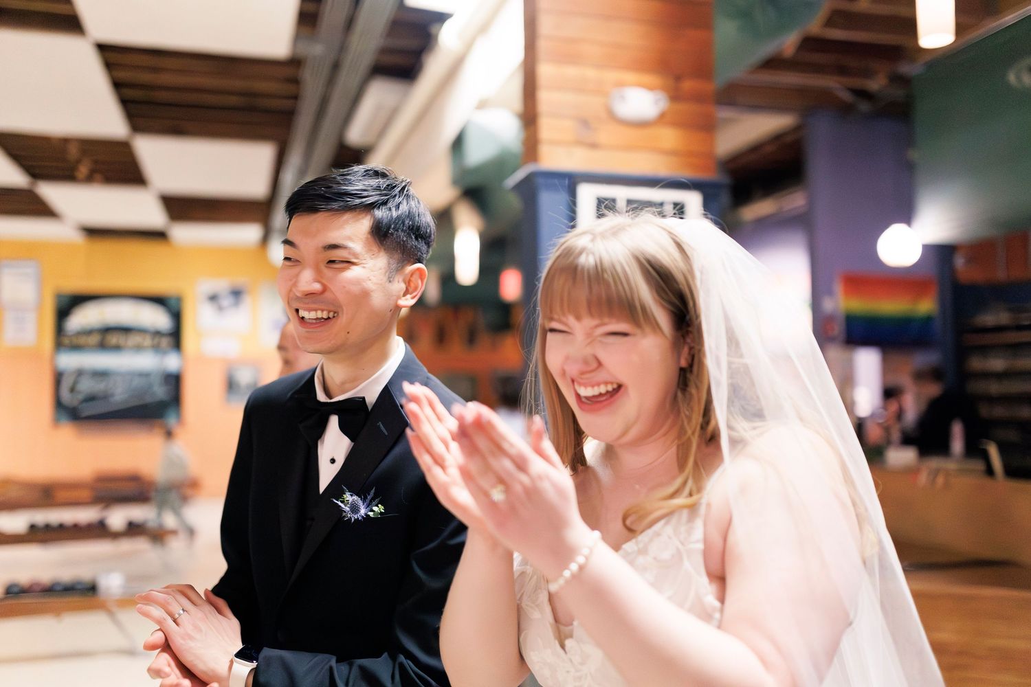 A happy couple in formal wedding attire share joyful moments and laughter at a bowling alley.