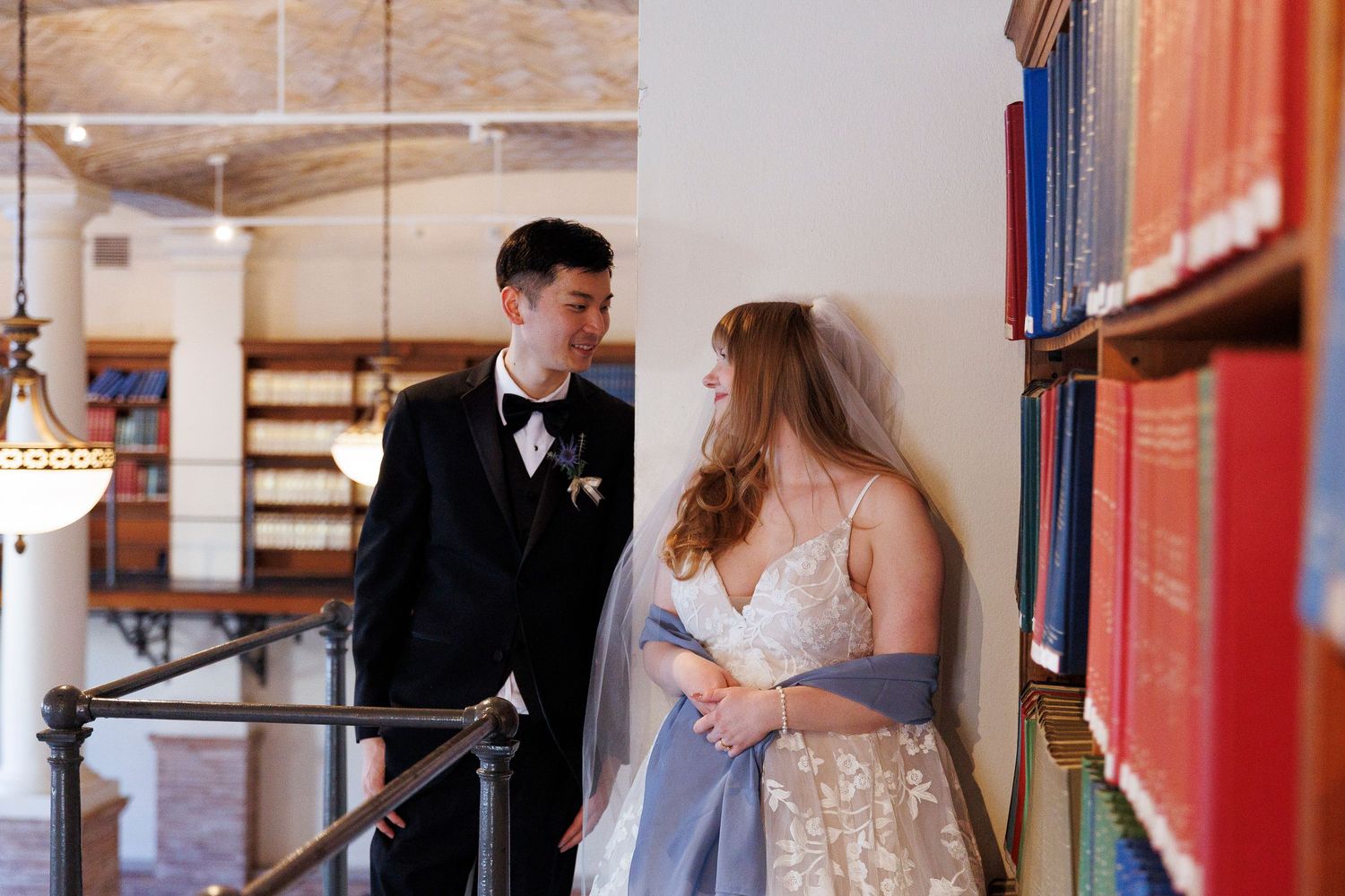 Bride and groom share a romantic moment beside colorful bookshelves in an elegant Boston Library wedding venue.