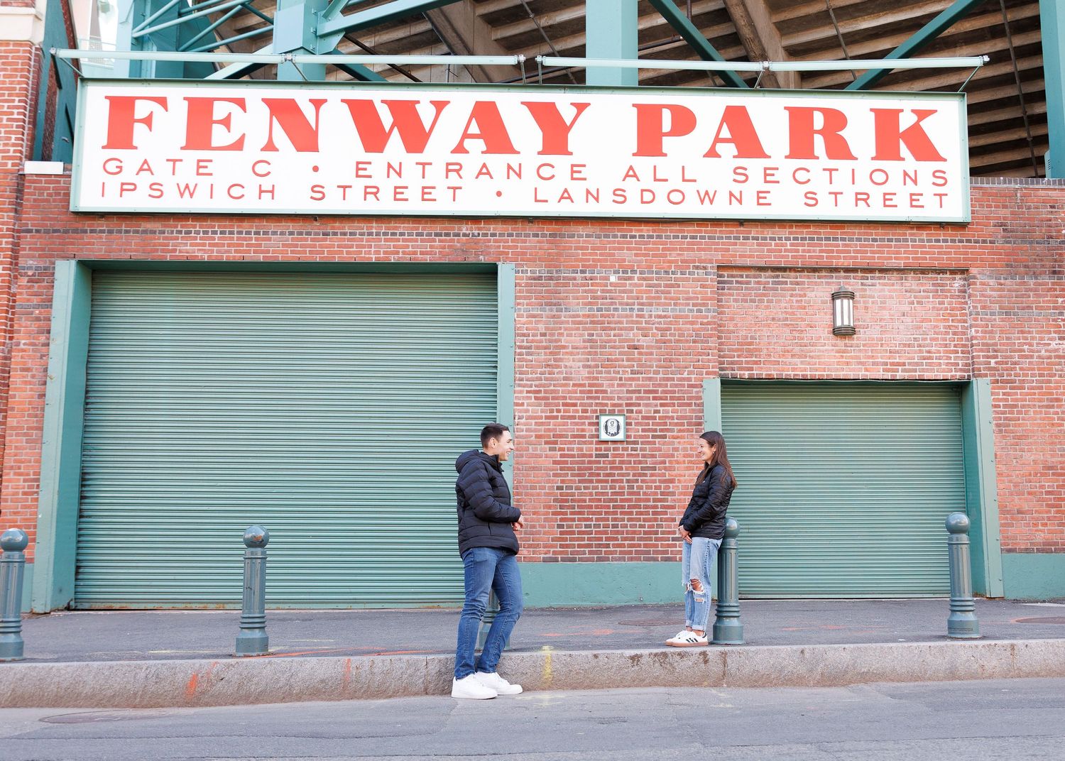 Two people stand outside Fenway Park Gate C on Lansdowne Street in Boston, Massachusetts.