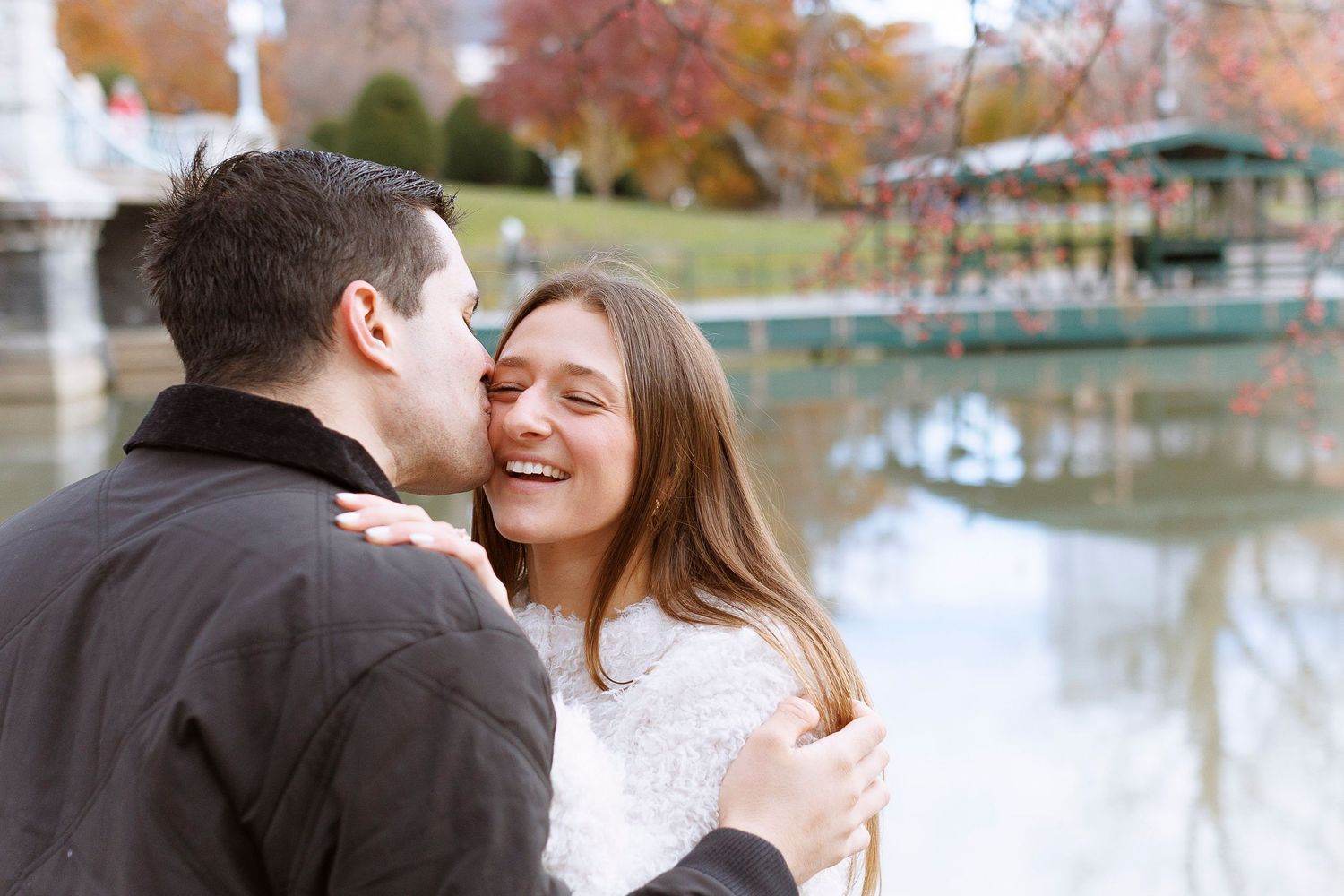 A couple shares romantic moments by a lake surrounded by autumn foliage on a fall afternoon at Boston Public Garden.