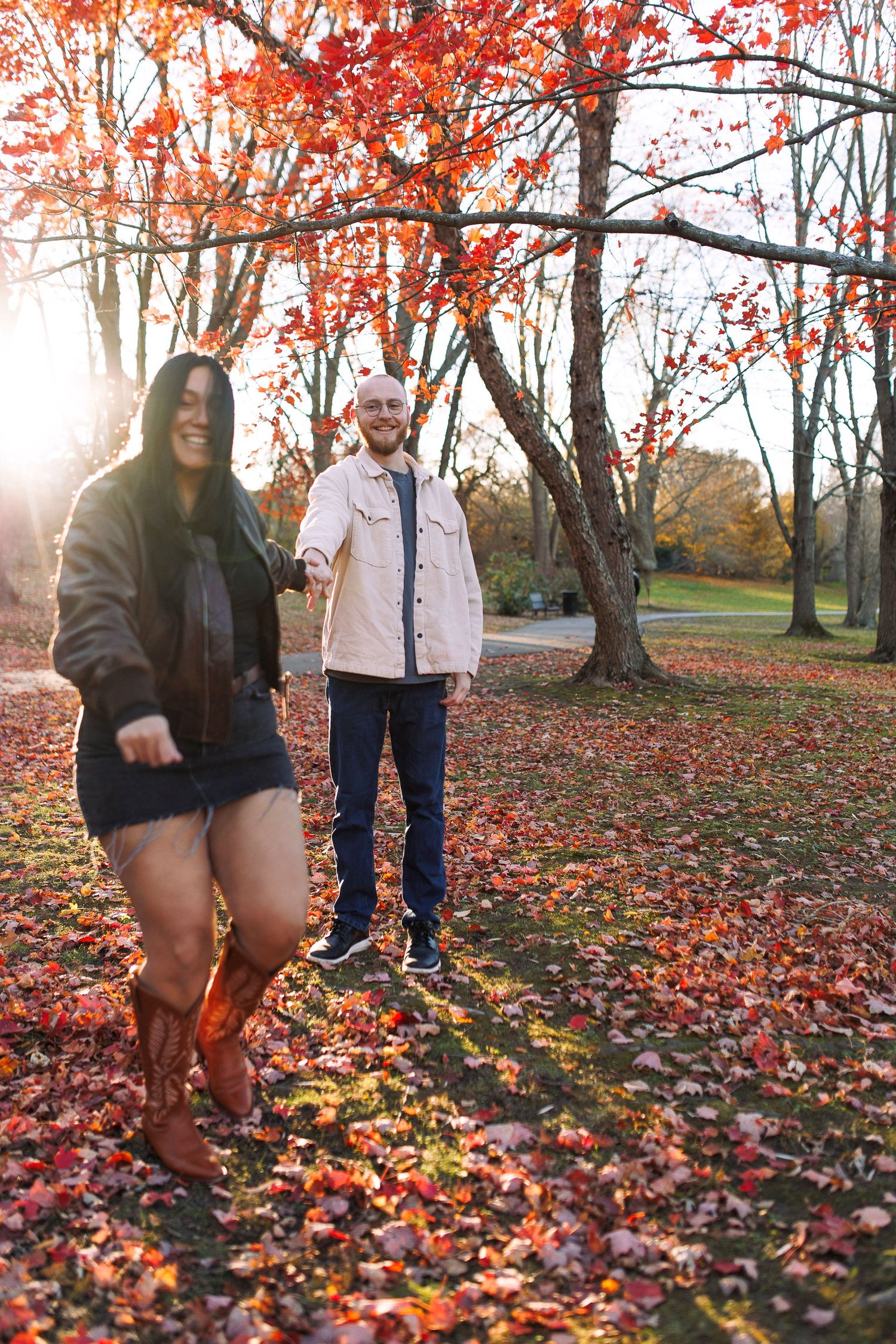 Two people enjoying a fall day among vibrant red maple trees and fallen leaves in at Larz Anderson park.