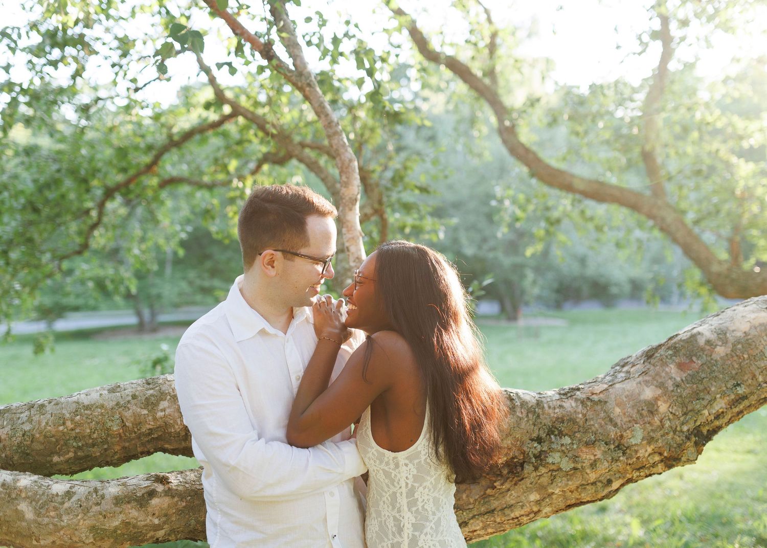 Romantic interracial couple sharing a tender moment under a tree in a sunlit green park.