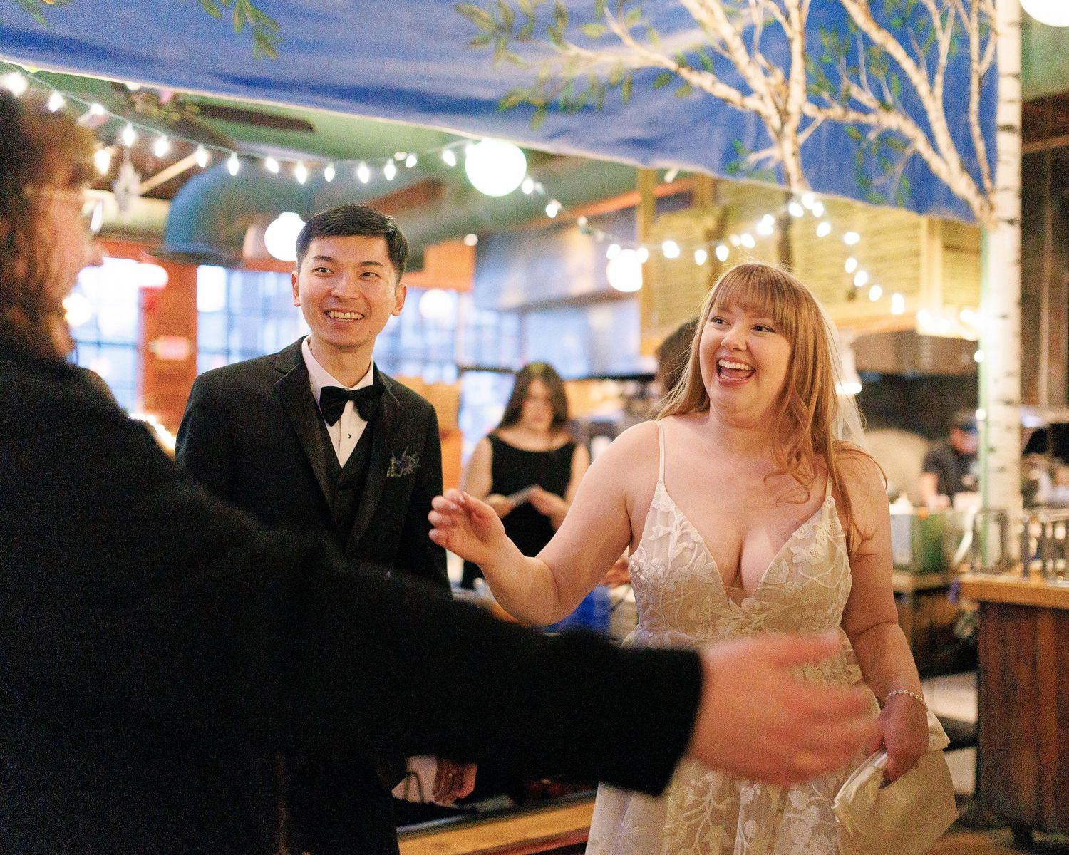 A couple celebrating and laughing together at a festive venue with string lights overhead.