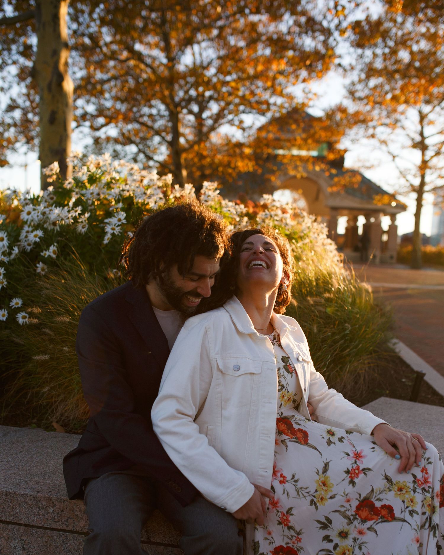 A couple shares joyful laughter while sitting together outdoors during golden hour sunset.