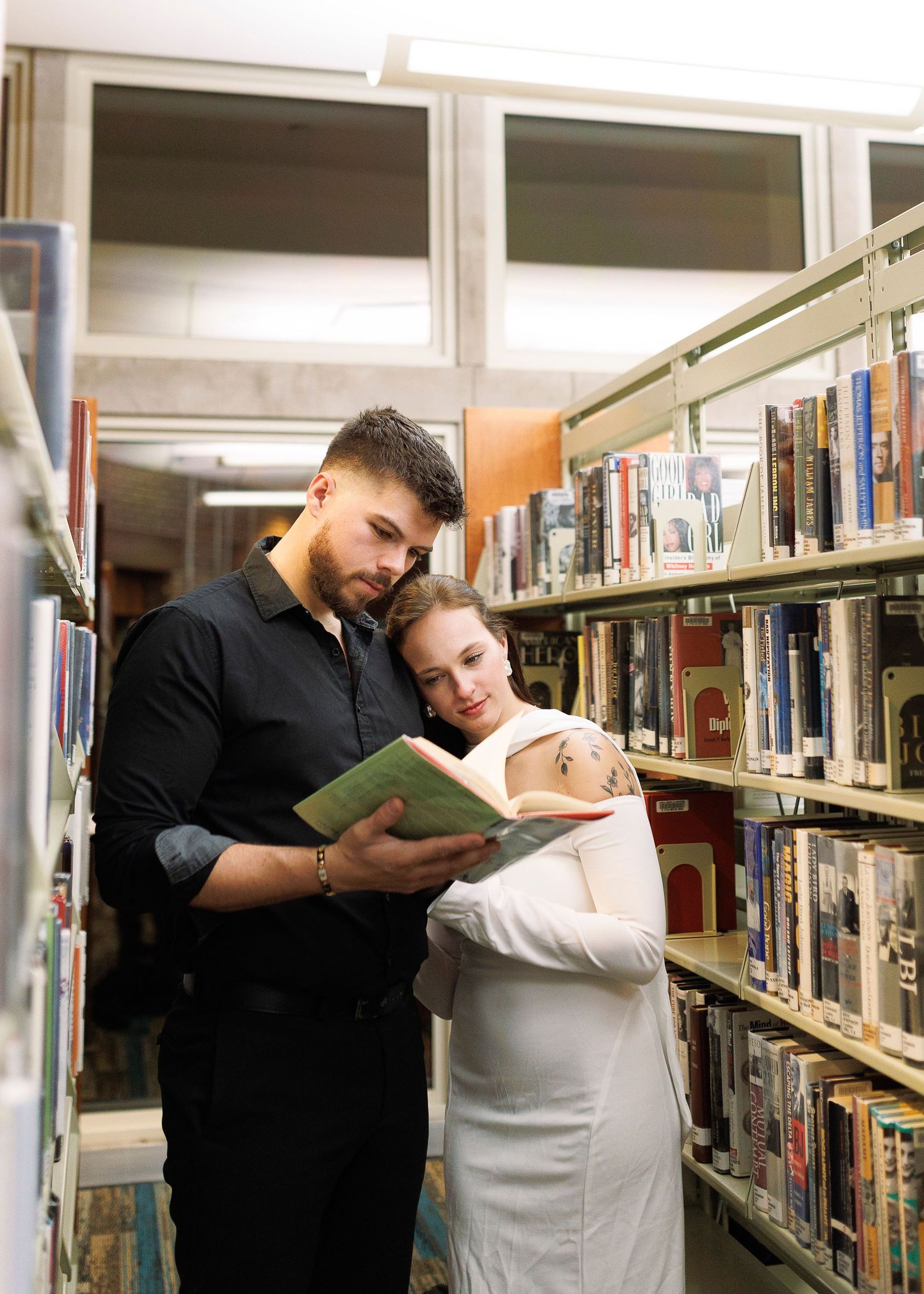 Students studying together in a library while leaning on bookshelves and reading from large books.