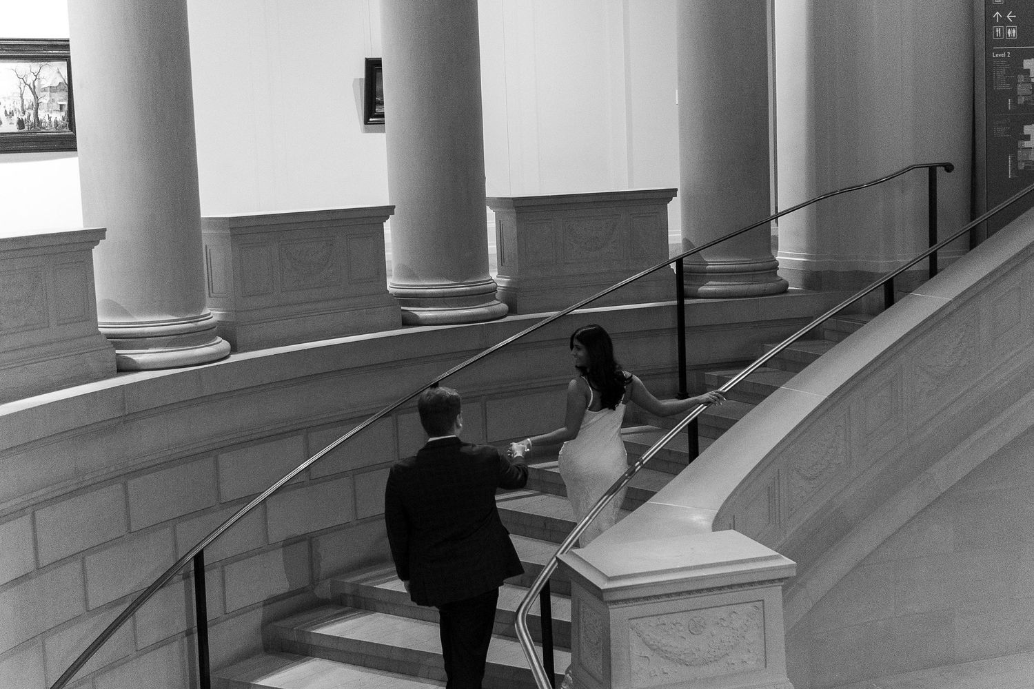 Black and white architectural interior with white columns and arches creating a dramatic perspective along a hallway.