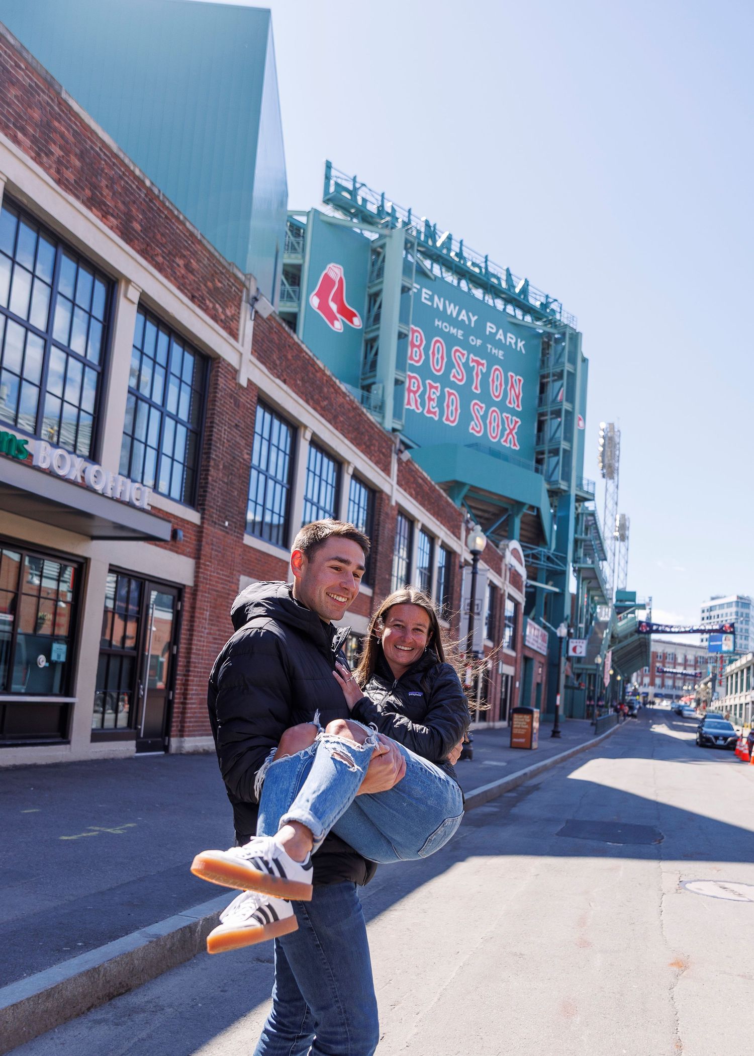 Couple posing playfully outside Fenway Park, home of the Boston Red Sox, on a sunny day in Boston, MA.
