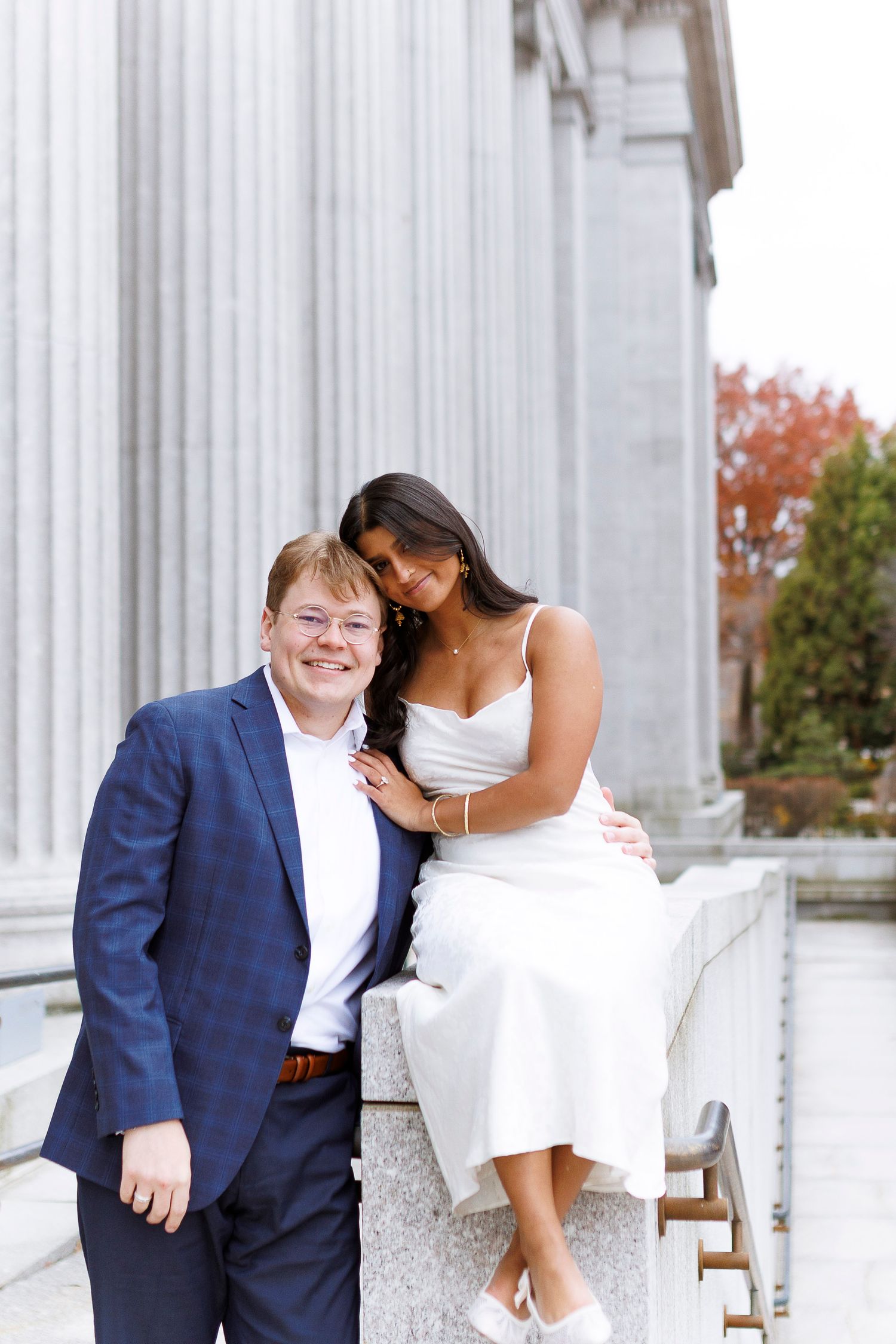 A couple poses together on white marble steps near classical columns during a romantic photoshoot.