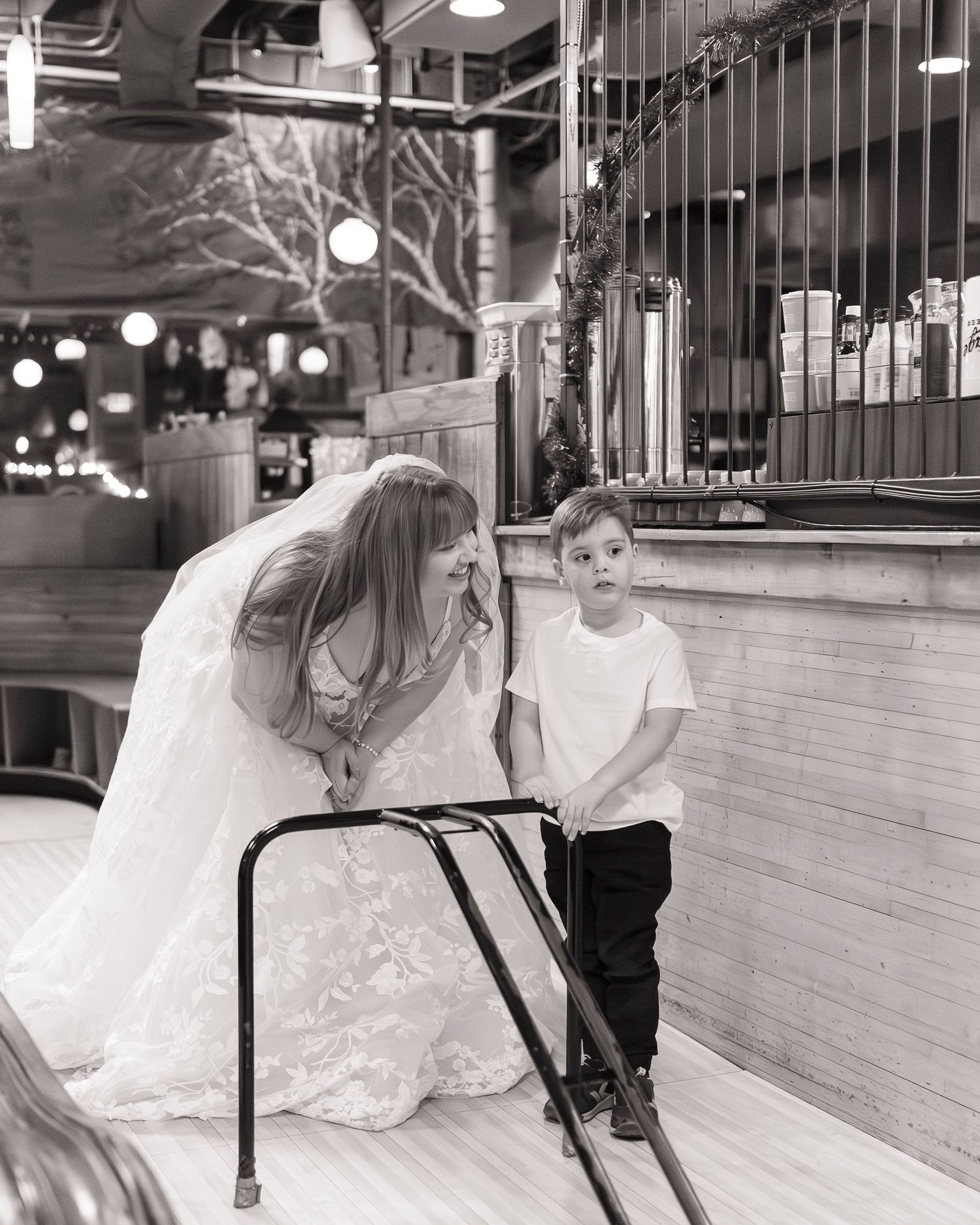A bride in an elegant white gown sits at a bar counter in black and white photography at Flatbreads in Somerville.