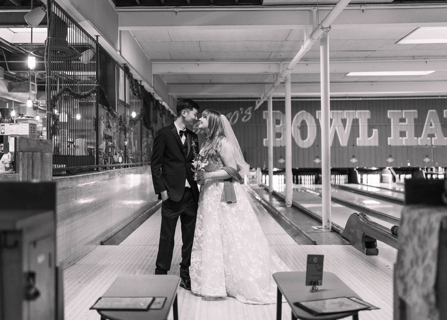 Black and white photo of a bride and groom kissing at a bowling alley wedding venue.