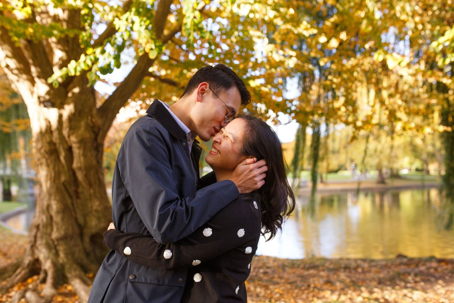 A romantic autumn moment shared between a couple embracing by a lake with golden fall foliage in the background.