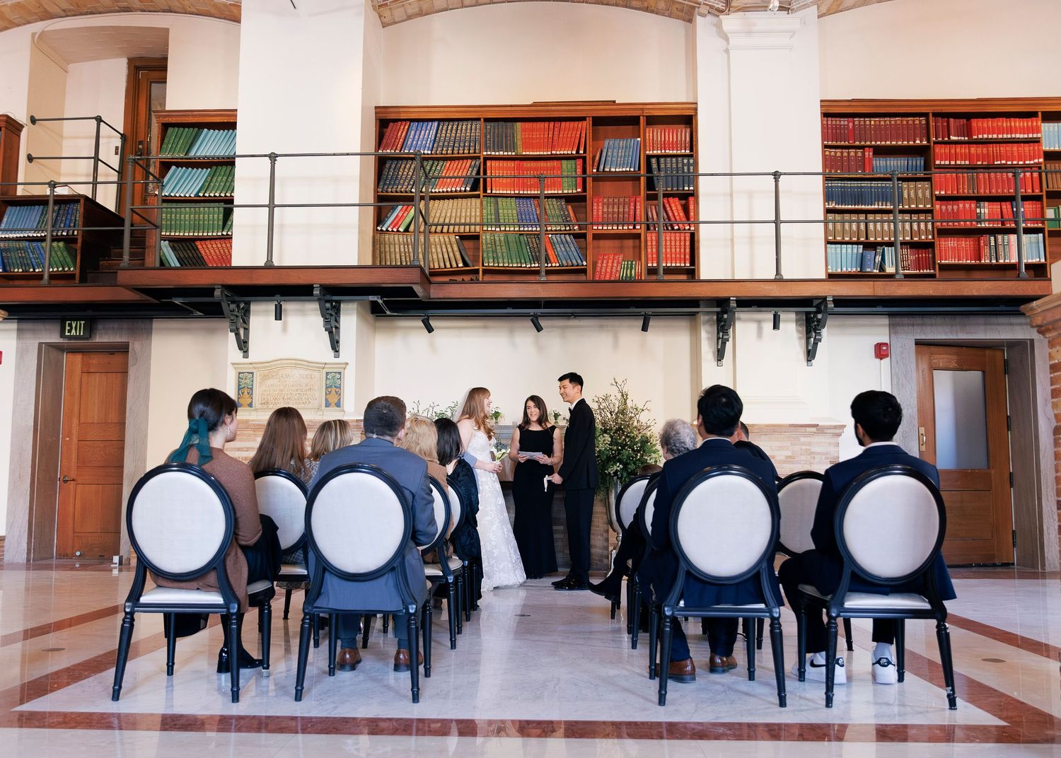 Small intimate wedding ceremony in a library with guests seated in elegant chairs.