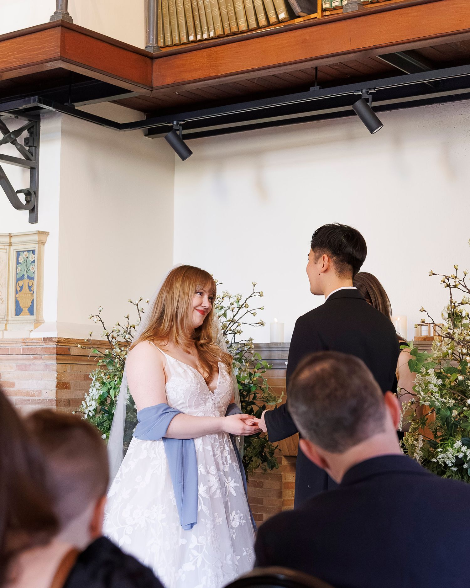 A couple exchanges vows during an intimate indoor ceremony with floral decorations and wooden accents.