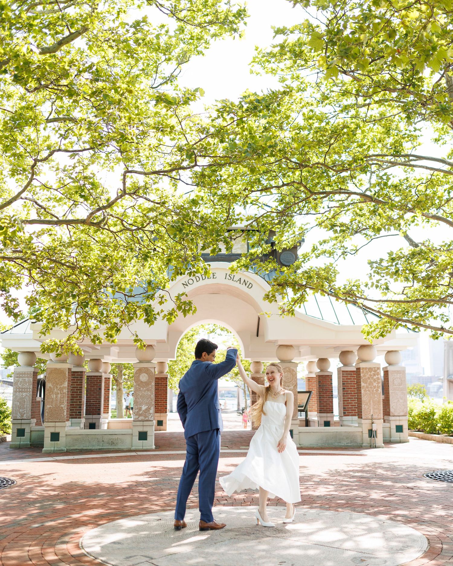 Couple dancing under trees at Governors Island pavilion on a sunny day.