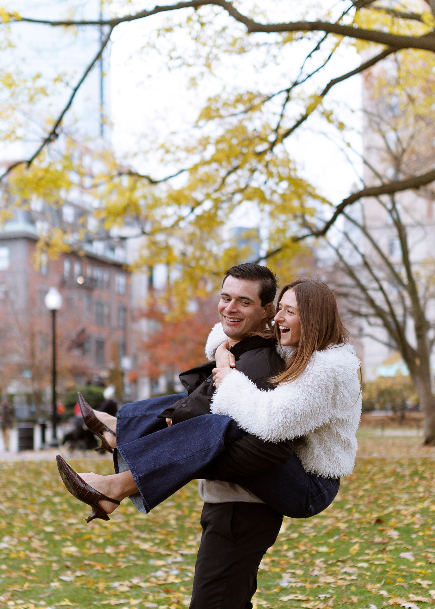 A couple playfully spins around in autumn leaves on a park path during a fall day.