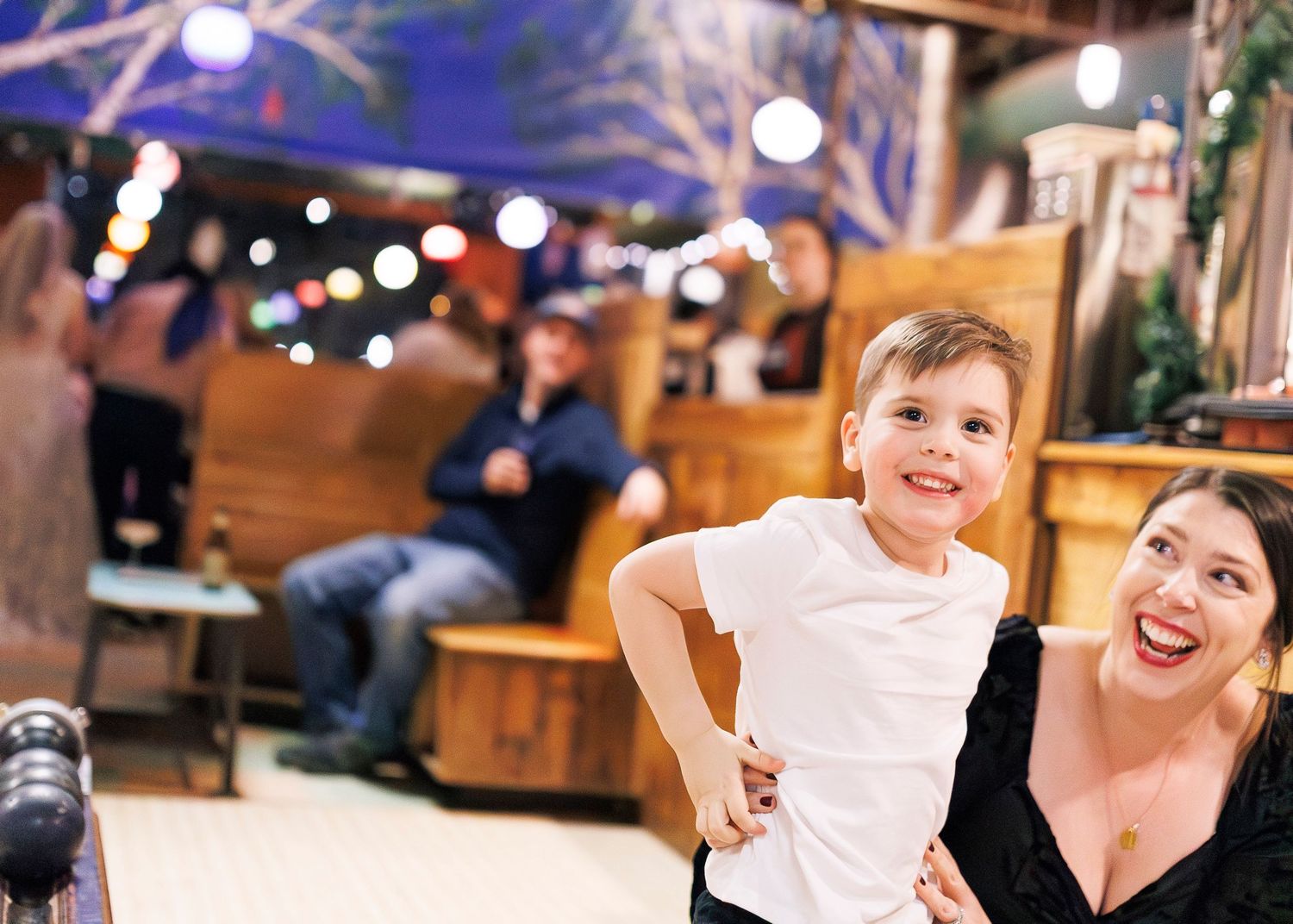 Happy mother and child share joyful moments at an indoor venue with festive lighting and decorations.