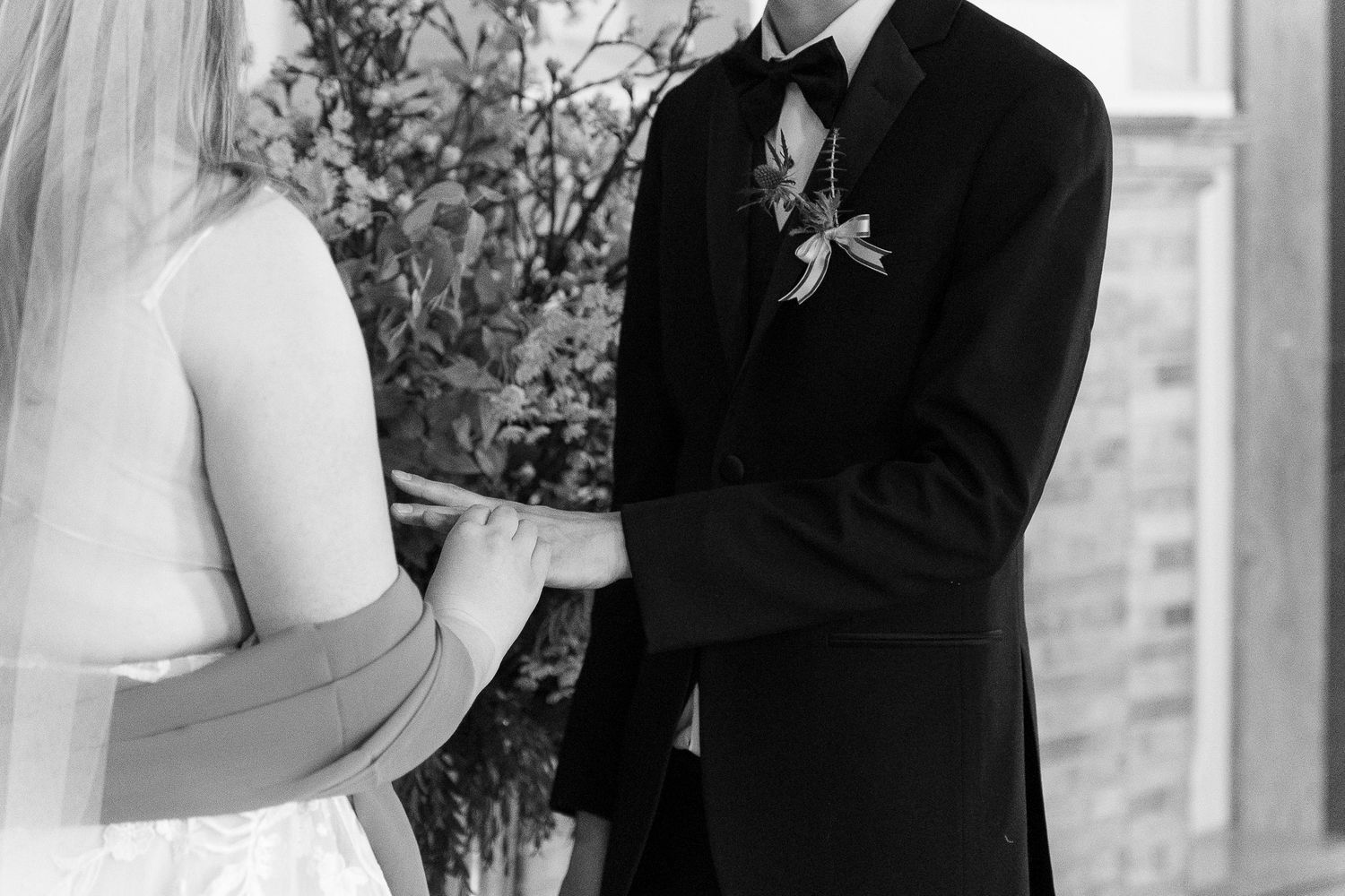 Black and white wedding ceremony photo showing a couple exchanging rings during their vows at the altar.