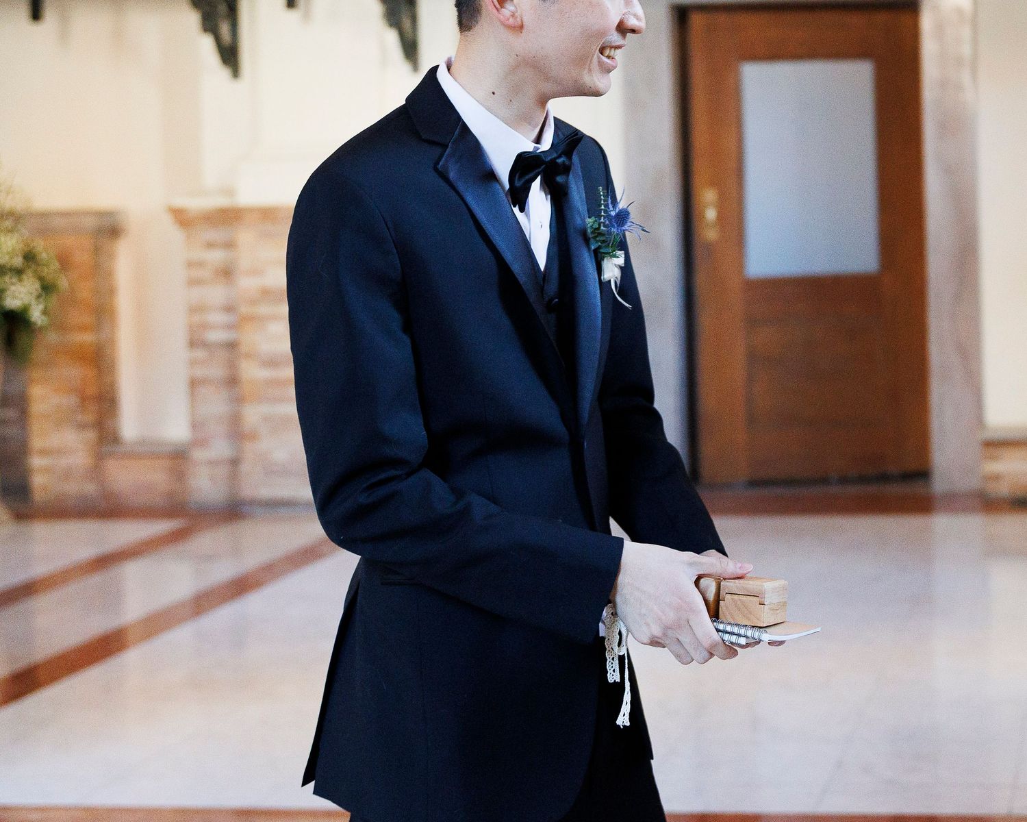 A person in a dark suit walks down a hallway while looking at their smartphone device.