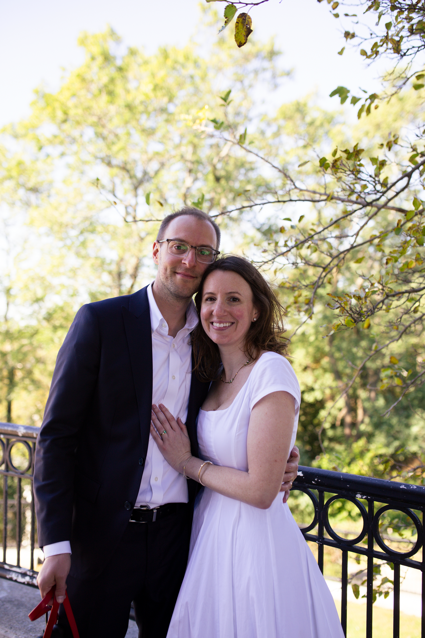 A couple in formal attire shares romantic moments on a balcony with lush greenery in the background.