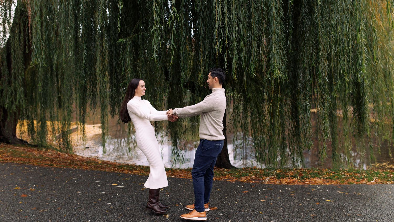 A couple shares a romantic moment under weeping willow trees in an outdoor garden setting.