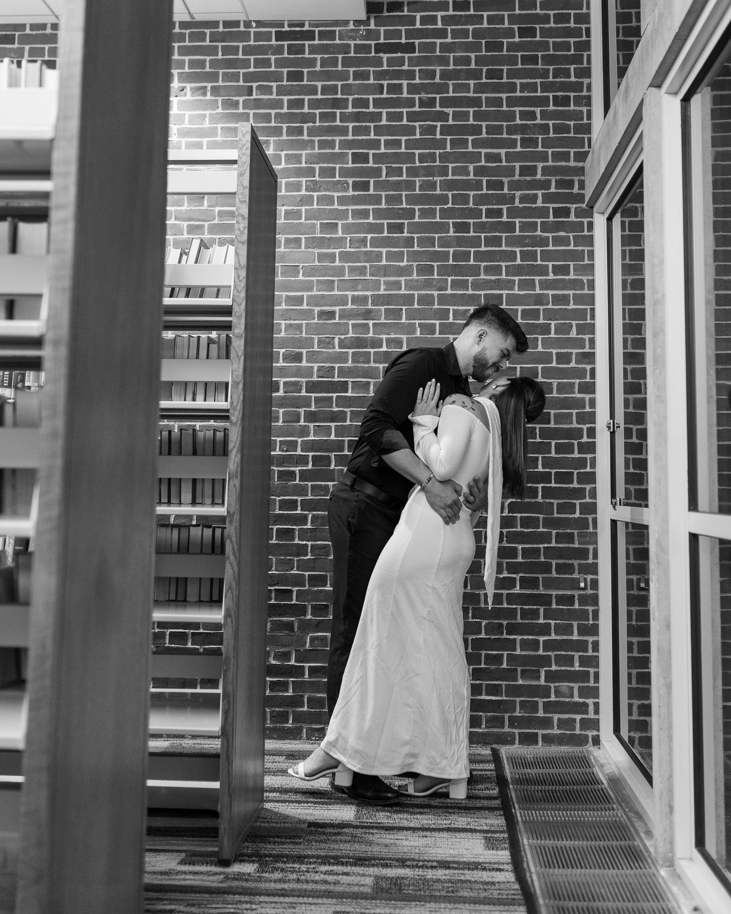 A black and white photograph shows someone leaning against a brick wall in a dramatic pose near windows.