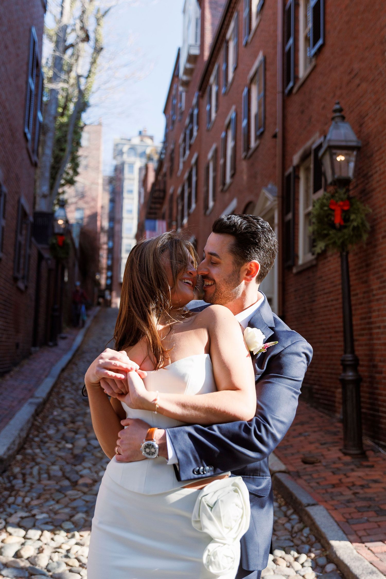 A couple shares a romantic kiss on a historic cobblestone street lined with brick buildings in Boston's Beacon Hill.