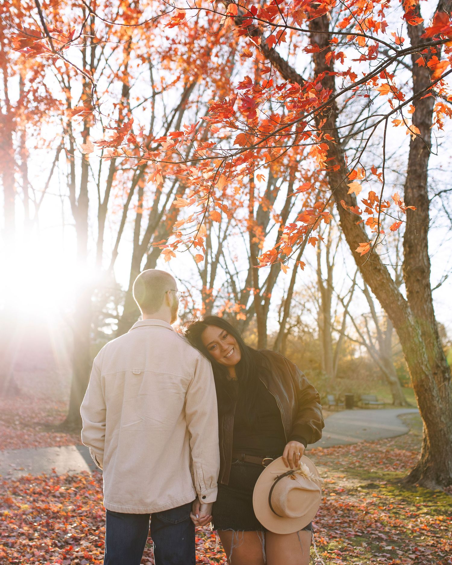 Romantic couple walking through misty autumn forest with vibrant orange foliage and sunlight streaming through trees at Larz Anderson park.