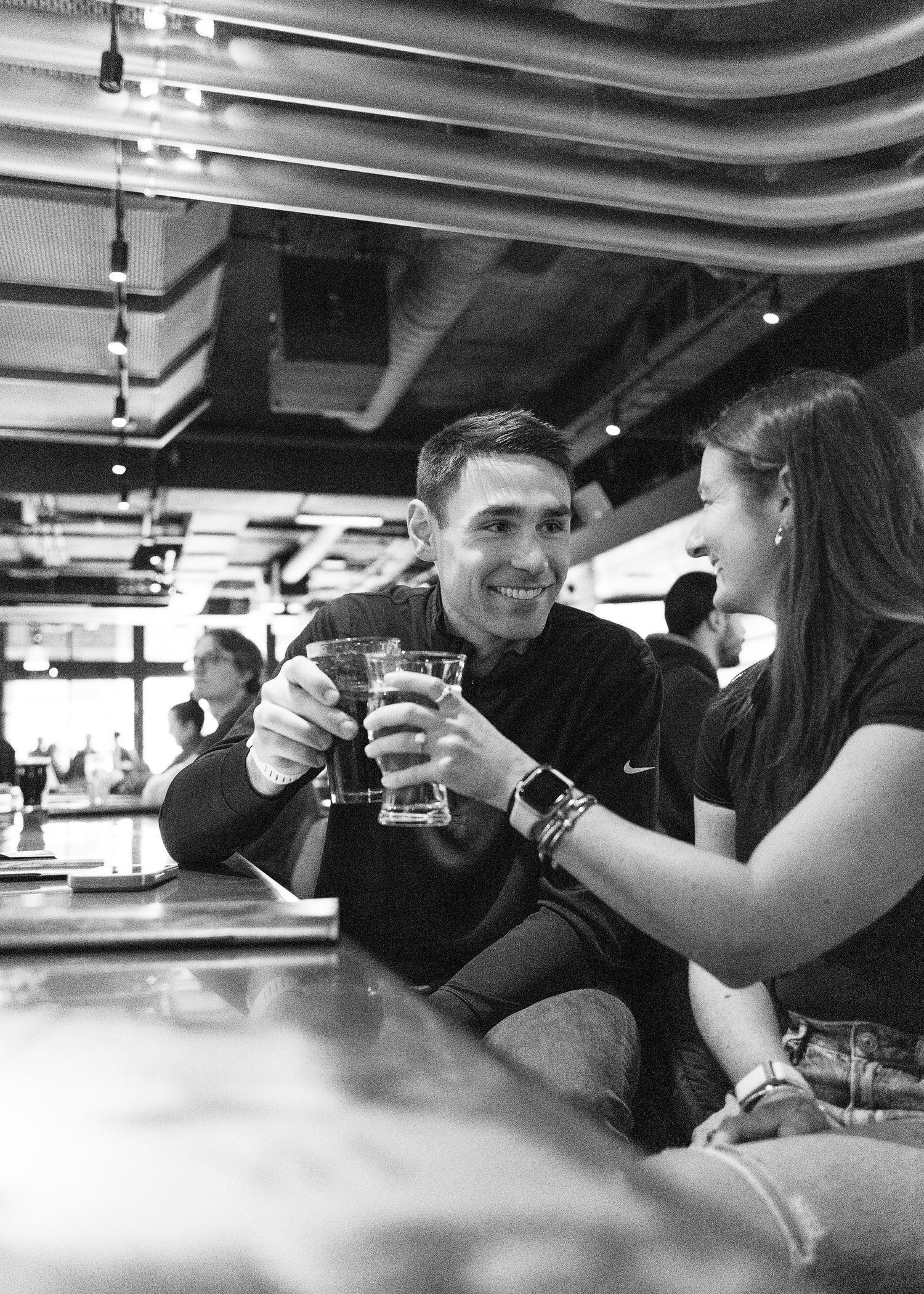 Smiling couple toasting with drinks at a bar near Fenway Park, black and white photo.