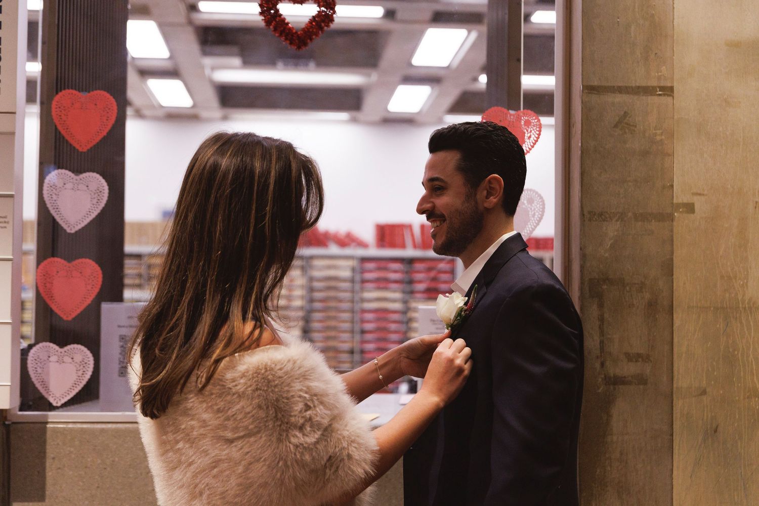 Couple sharing a romantic moment near Valentine's Day heart decorations, woman adjusting man's boutonniere.