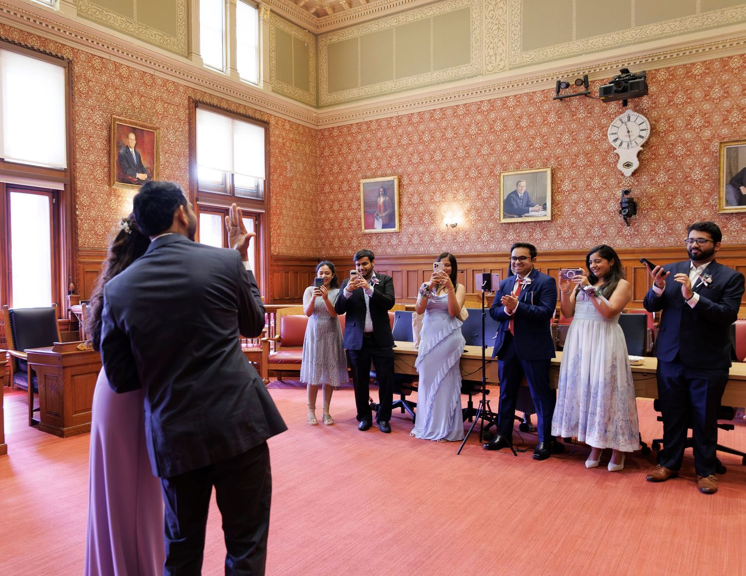 Group of professionals applauding in an elegant red-walled government chamber during a formal ceremony.