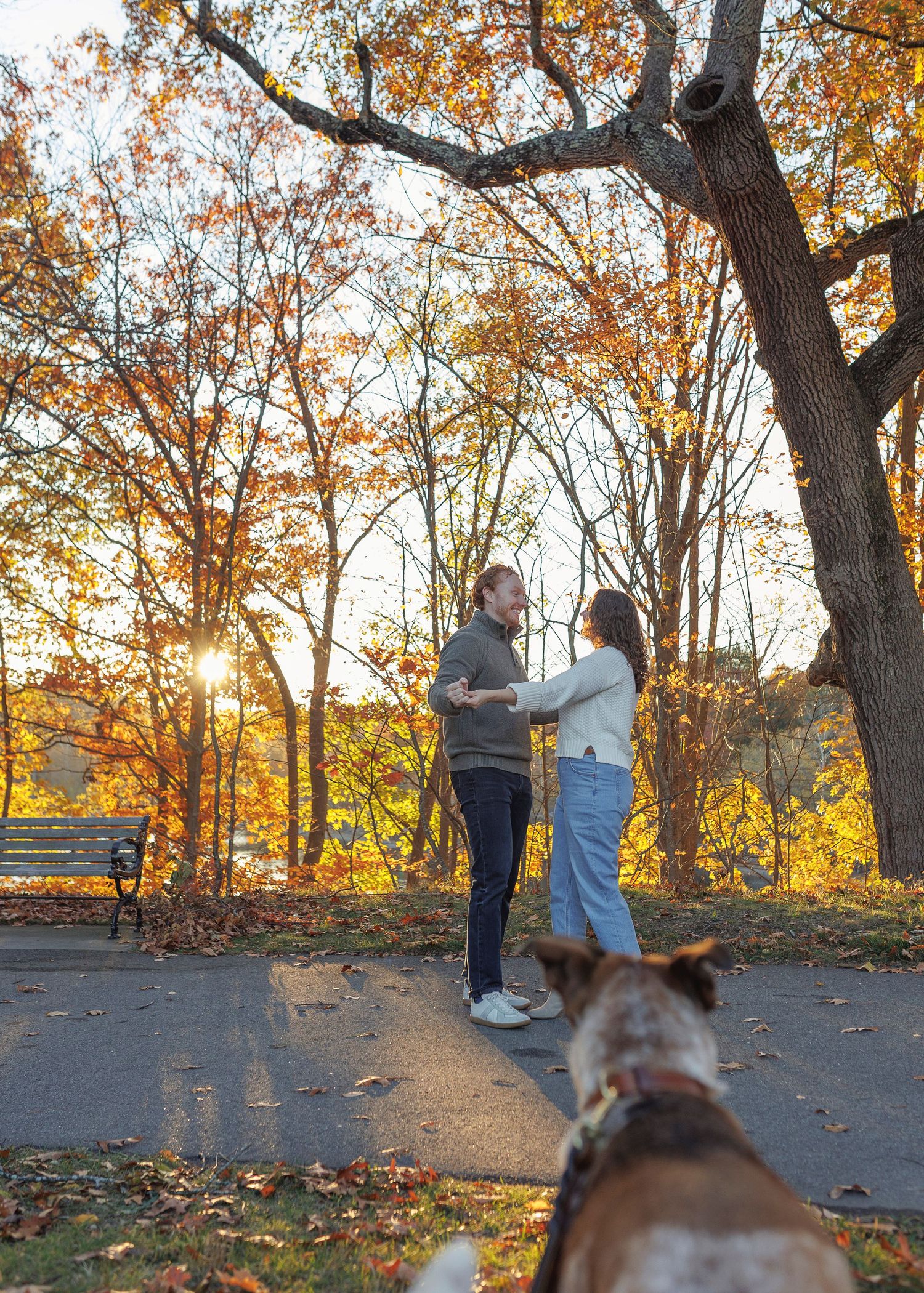 People walking on an autumn path with golden trees and fallen leaves during sunset in a park.