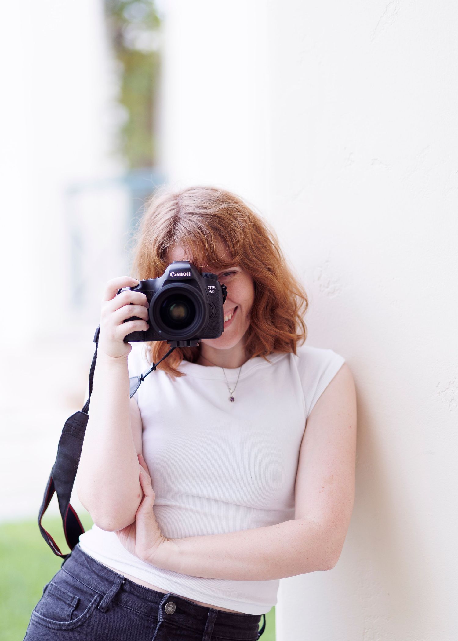 A photographer in a white sleeveless top takes photos with a DSLR camera in a bright indoor setting.