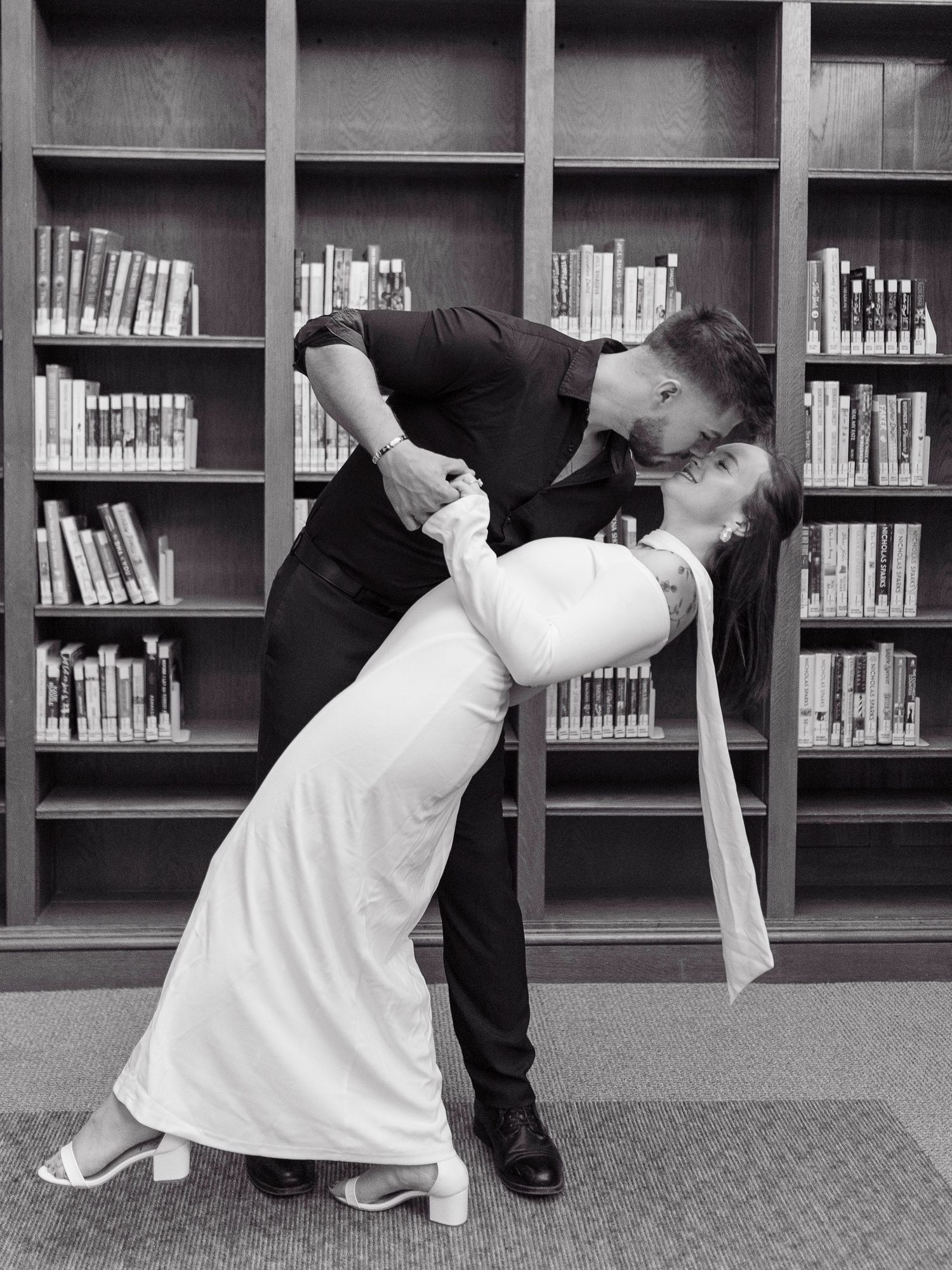A sequence of four black and white photos showing two people performing a dramatic dance move in front of library shelves.