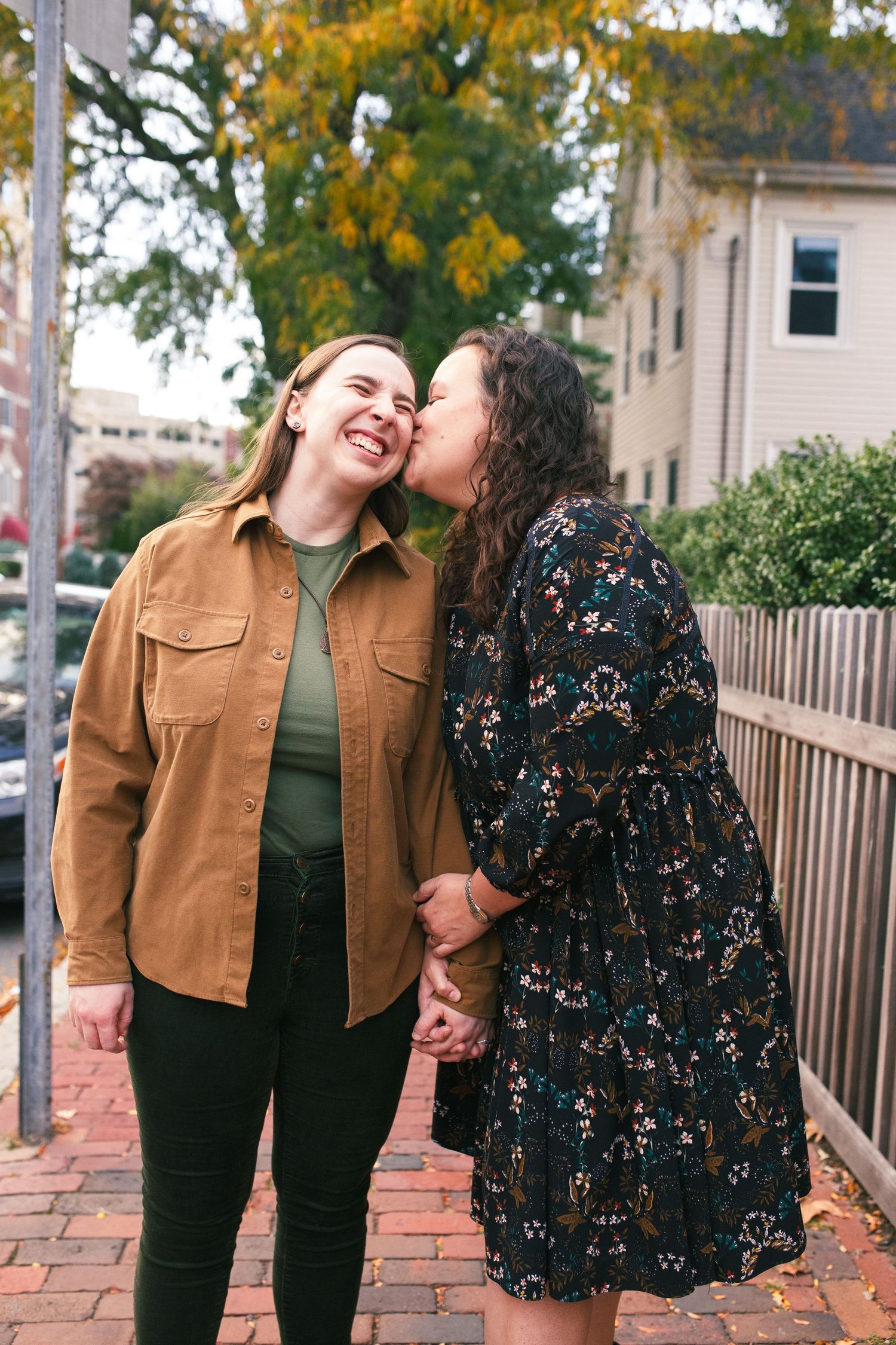 A couple shares a joyful moment together on a brick sidewalk during autumn, wearing casual fall attire.