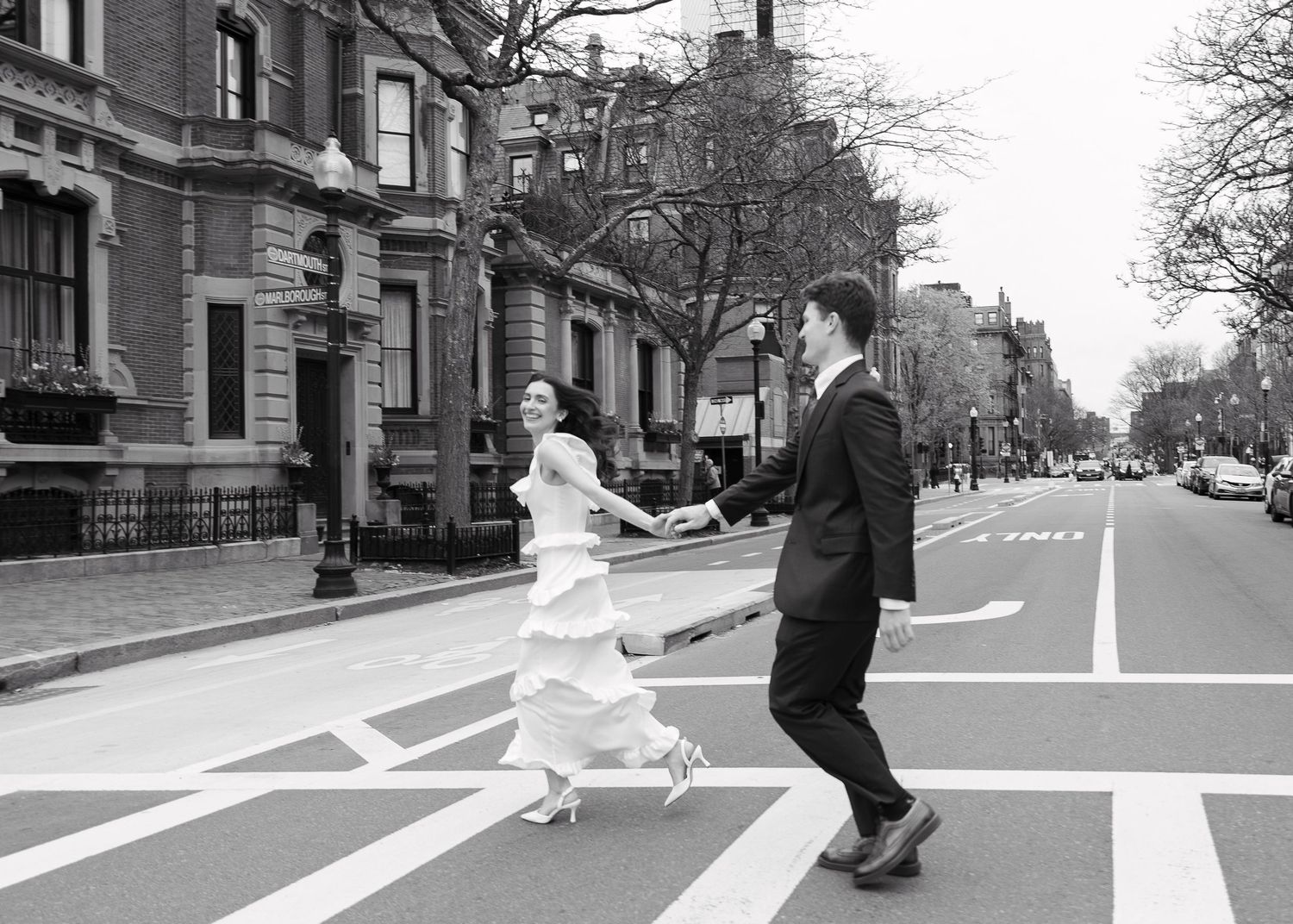 Black and white photo of a bride and groom holding hands crossing a street in Boston on their wedding day.