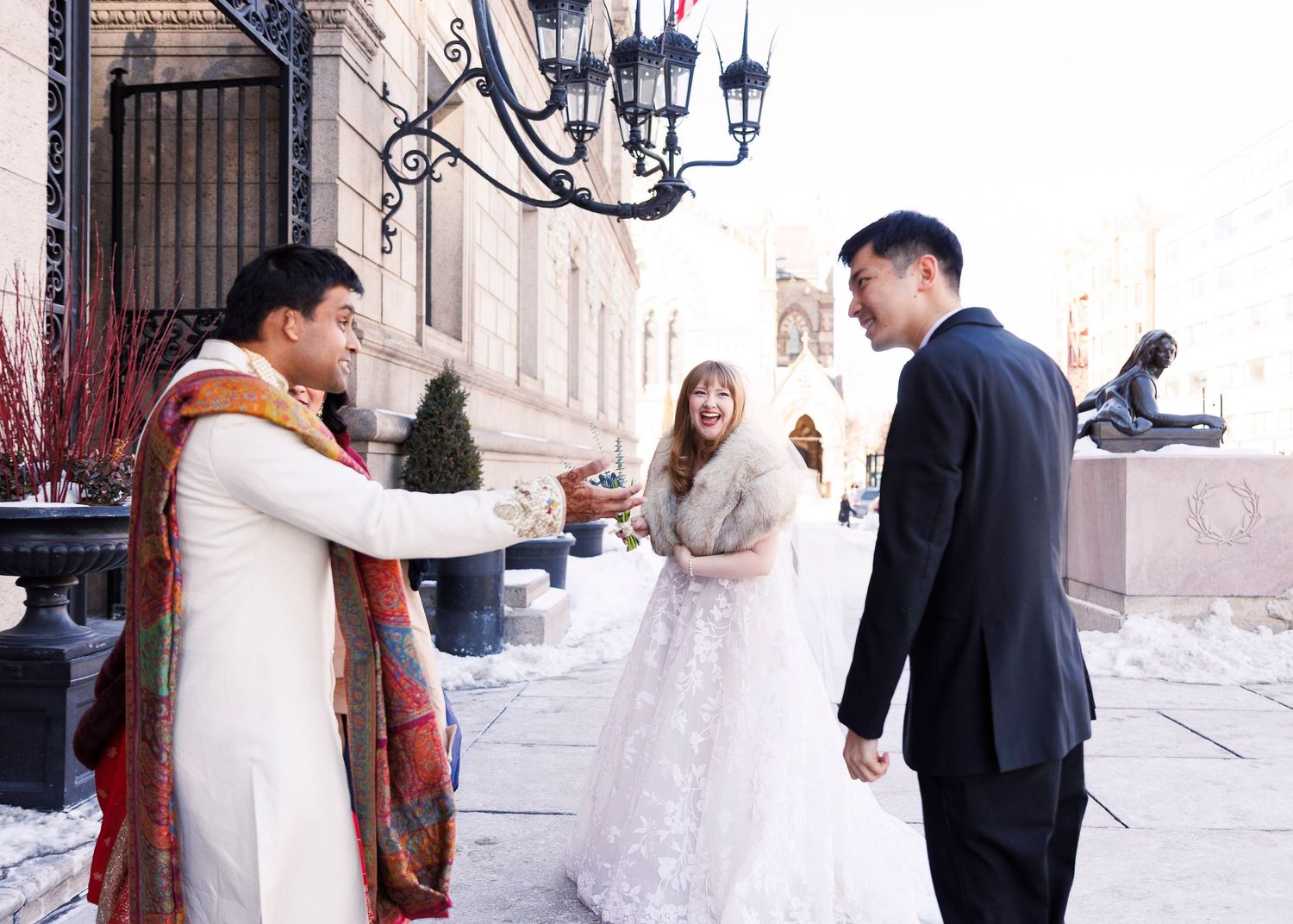 Two people embrace and smile while standing near decorative iron gates and stone architecture.