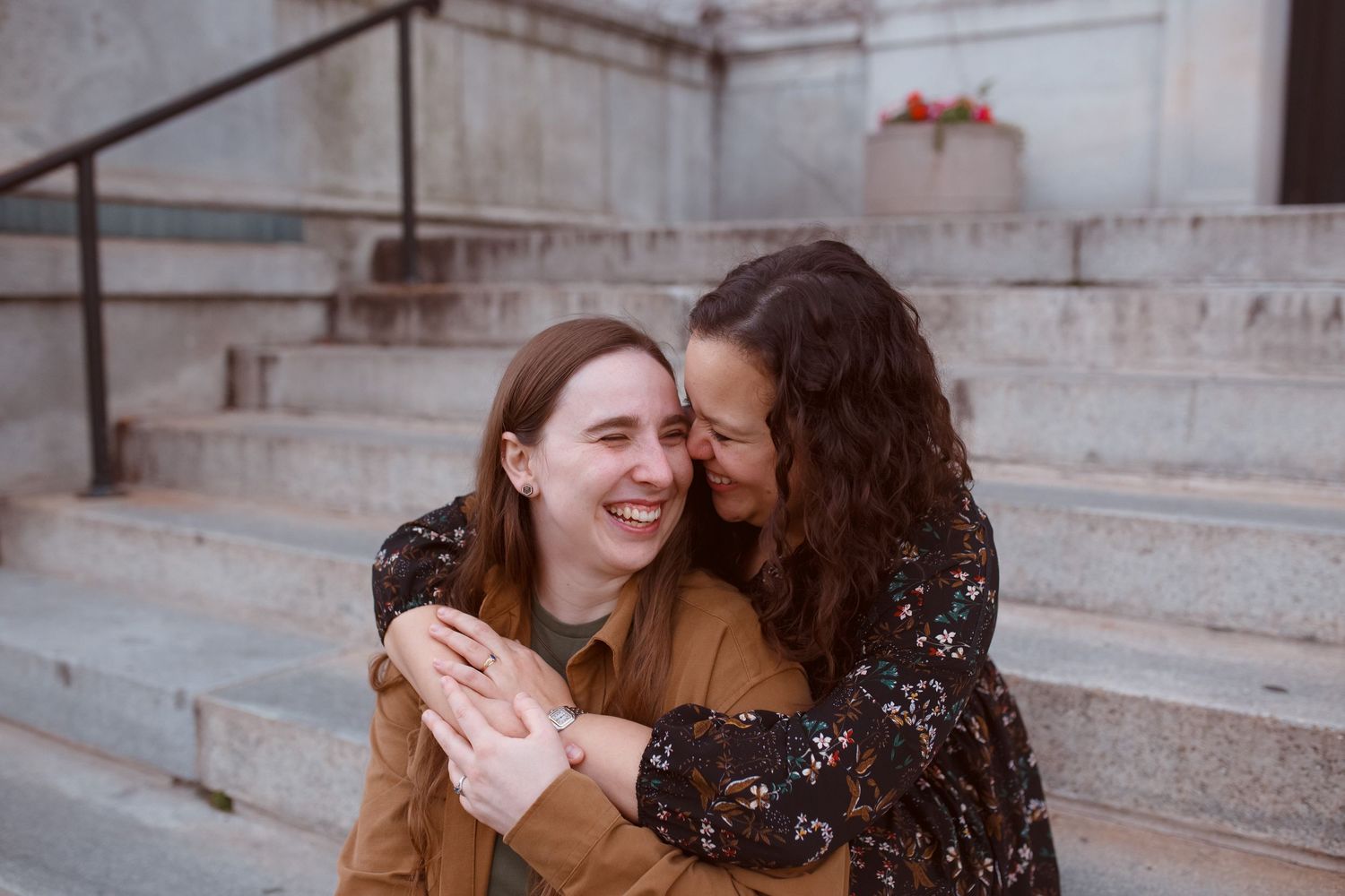 Two people share a joyful moment laughing together while sitting on concrete steps outdoors.