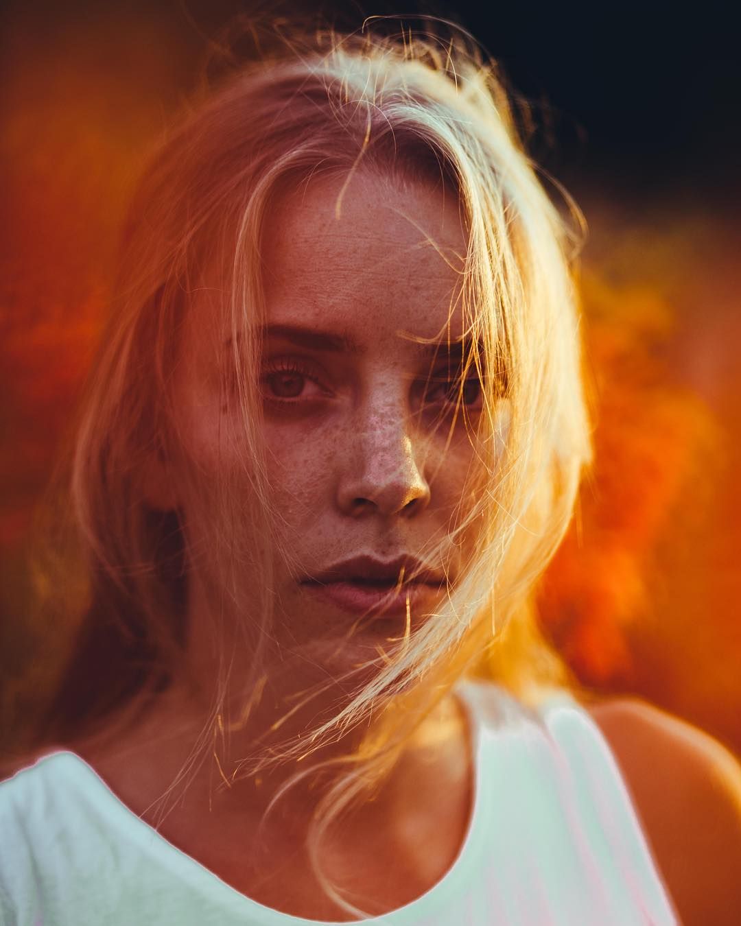 A series of warm-toned portraits with blonde hair in motion against a fiery orange and red background.