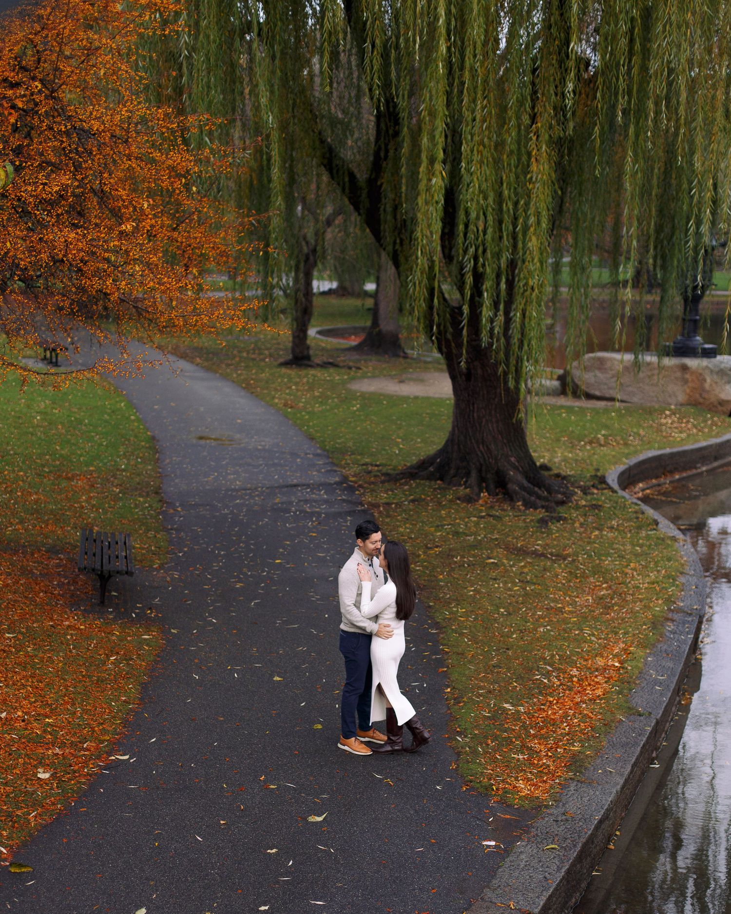 Boston couple dancing together under autumn trees along a park path with fallen orange leaves and weeping willows in Boston Public Garden.