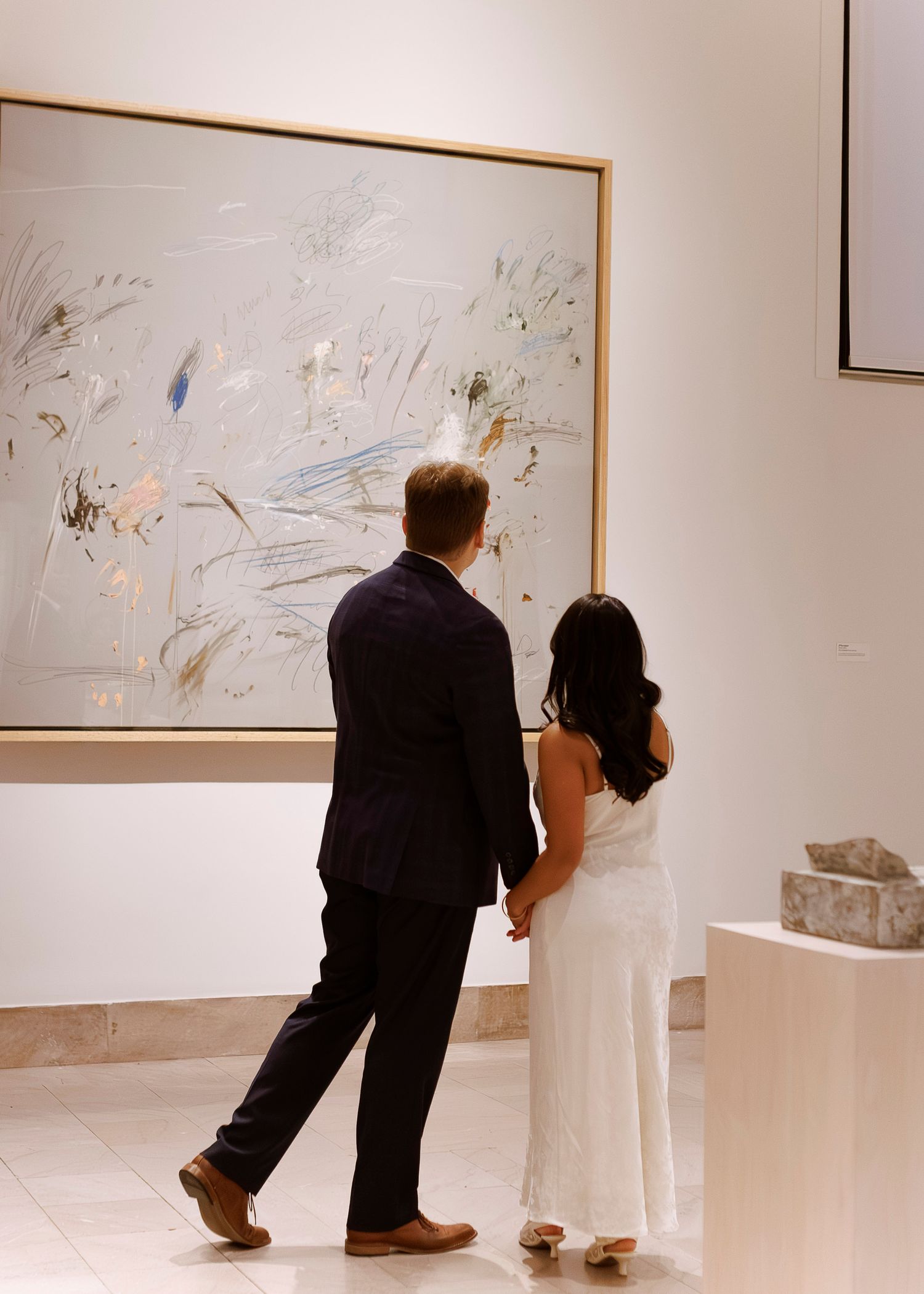 Gallery visitors examine abstract artwork displayed on white walls in a modern exhibition space.