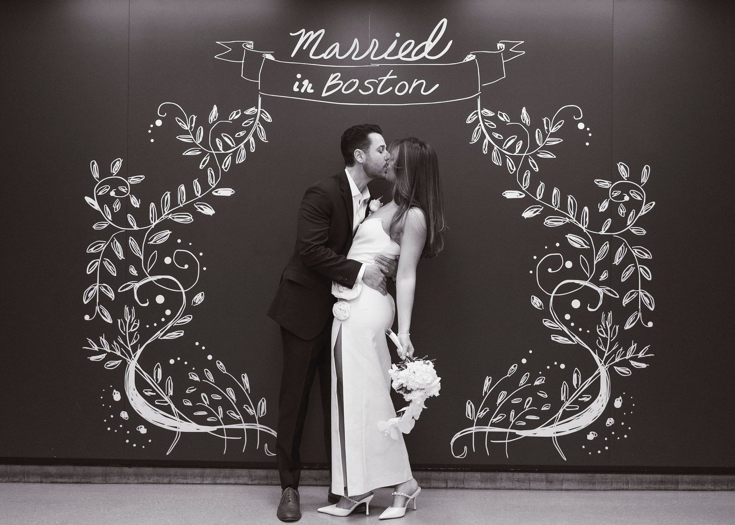 Couple kissing in front of a chalkboard sign reading Married in Boston, black and white wedding photo.
