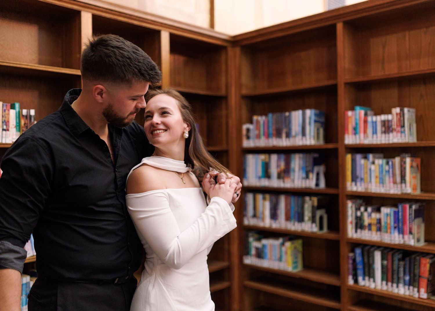 A romantic moment between a couple dancing in a library with wooden bookshelves in the background.