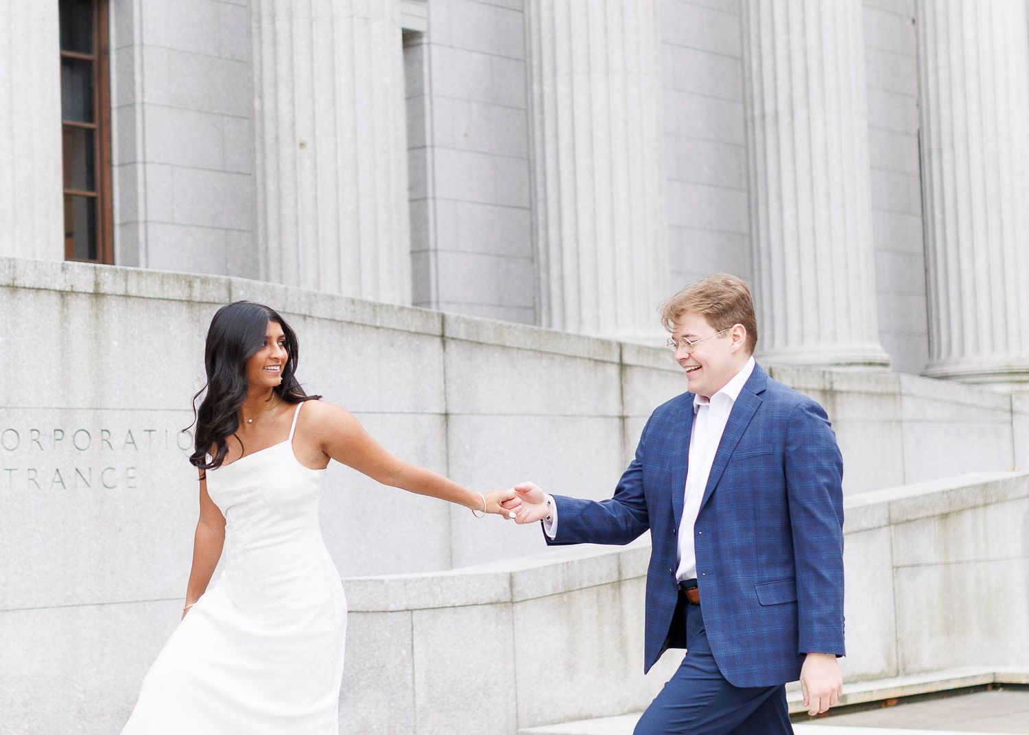 A wedding couple dances gracefully across a white marble colonnade outside a grand classical building.