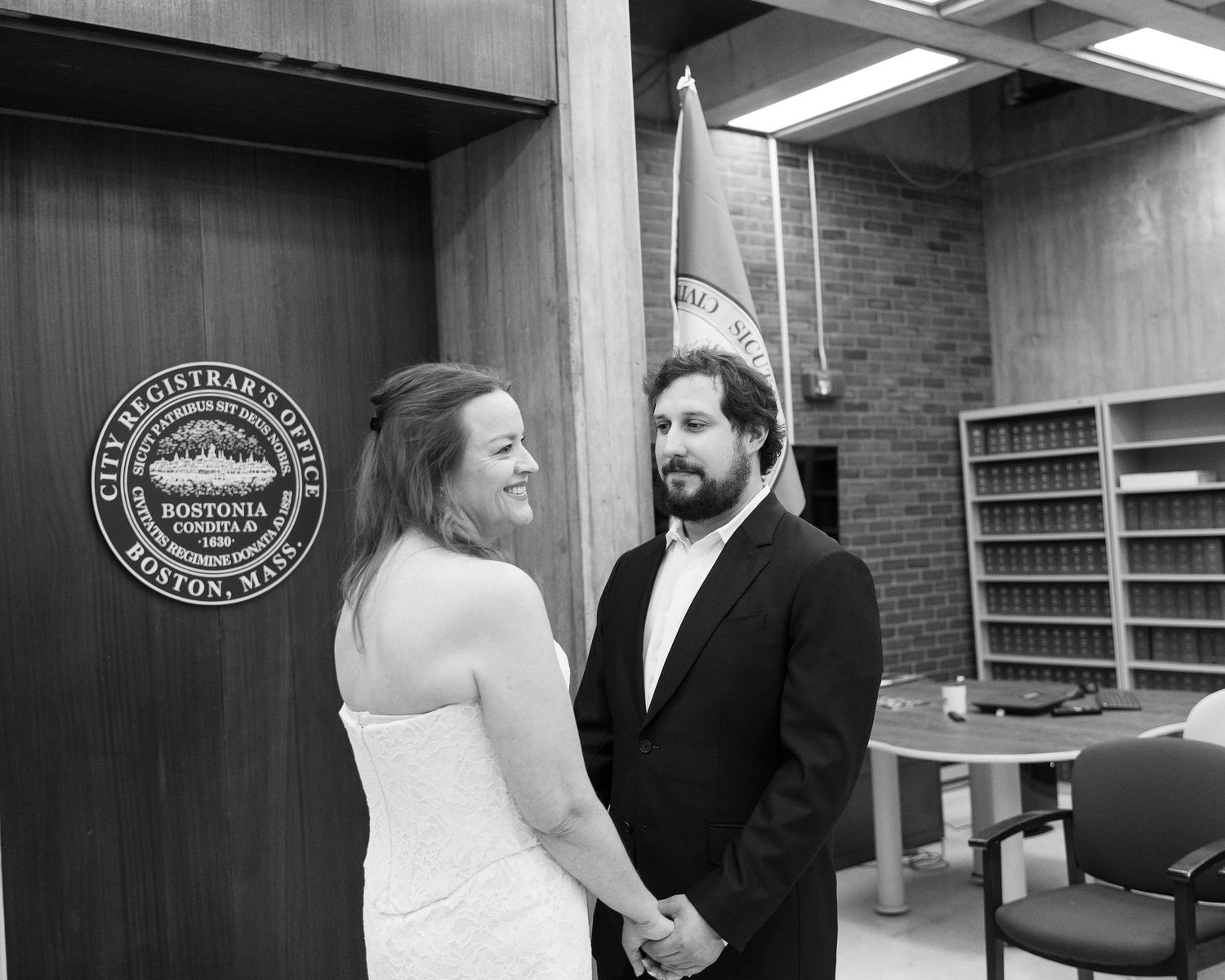 Couple holding hands at Boston City Hall Registrar office during a civil wedding ceremony, black and white photo.